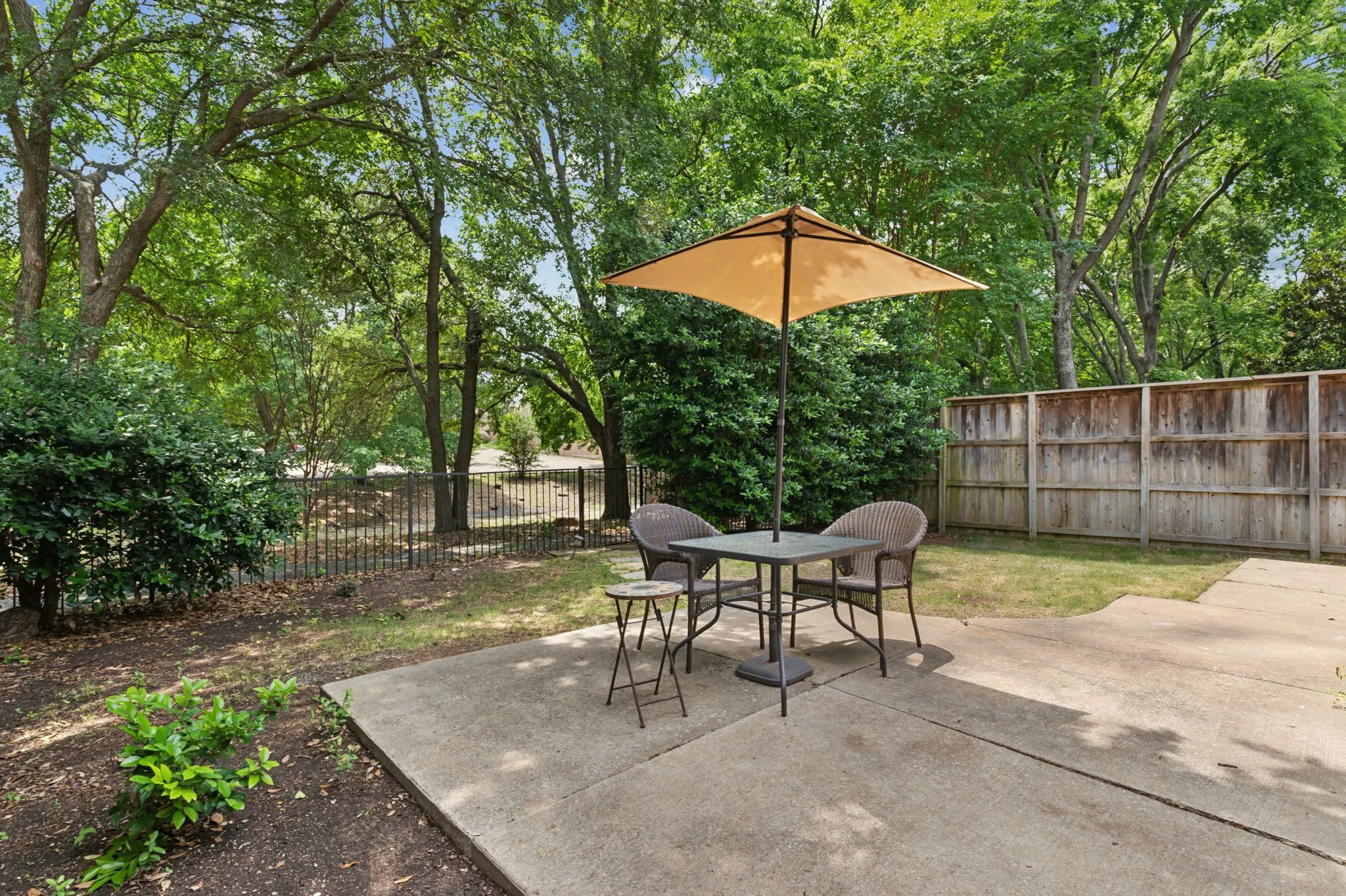 Concrete patio with an expansive fenced yard, mature trees, and privacy hedges