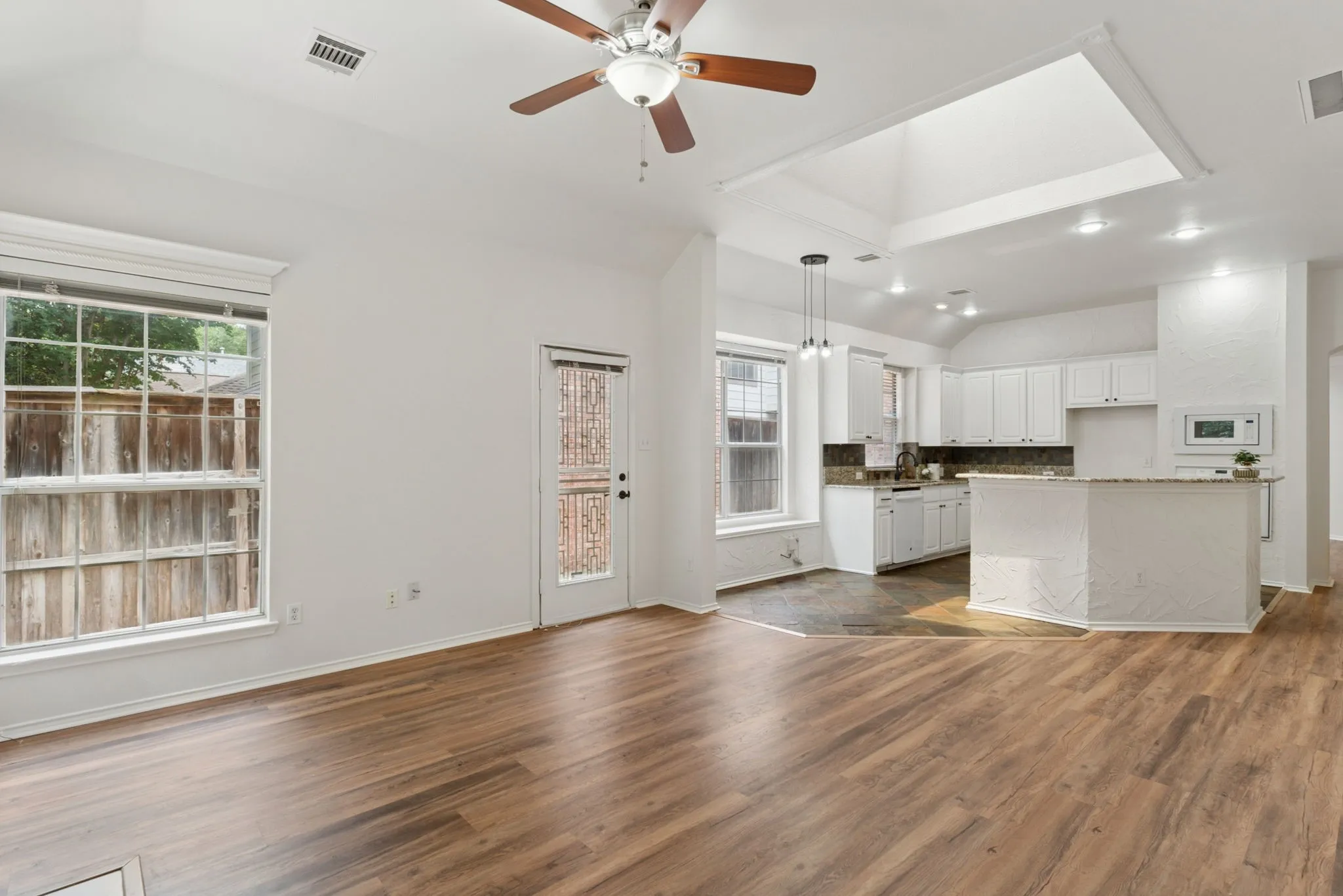 Wood-finish flooring, vaulted ceiling, ceiling fan, white cabinetry, and kitchen island with a countertop