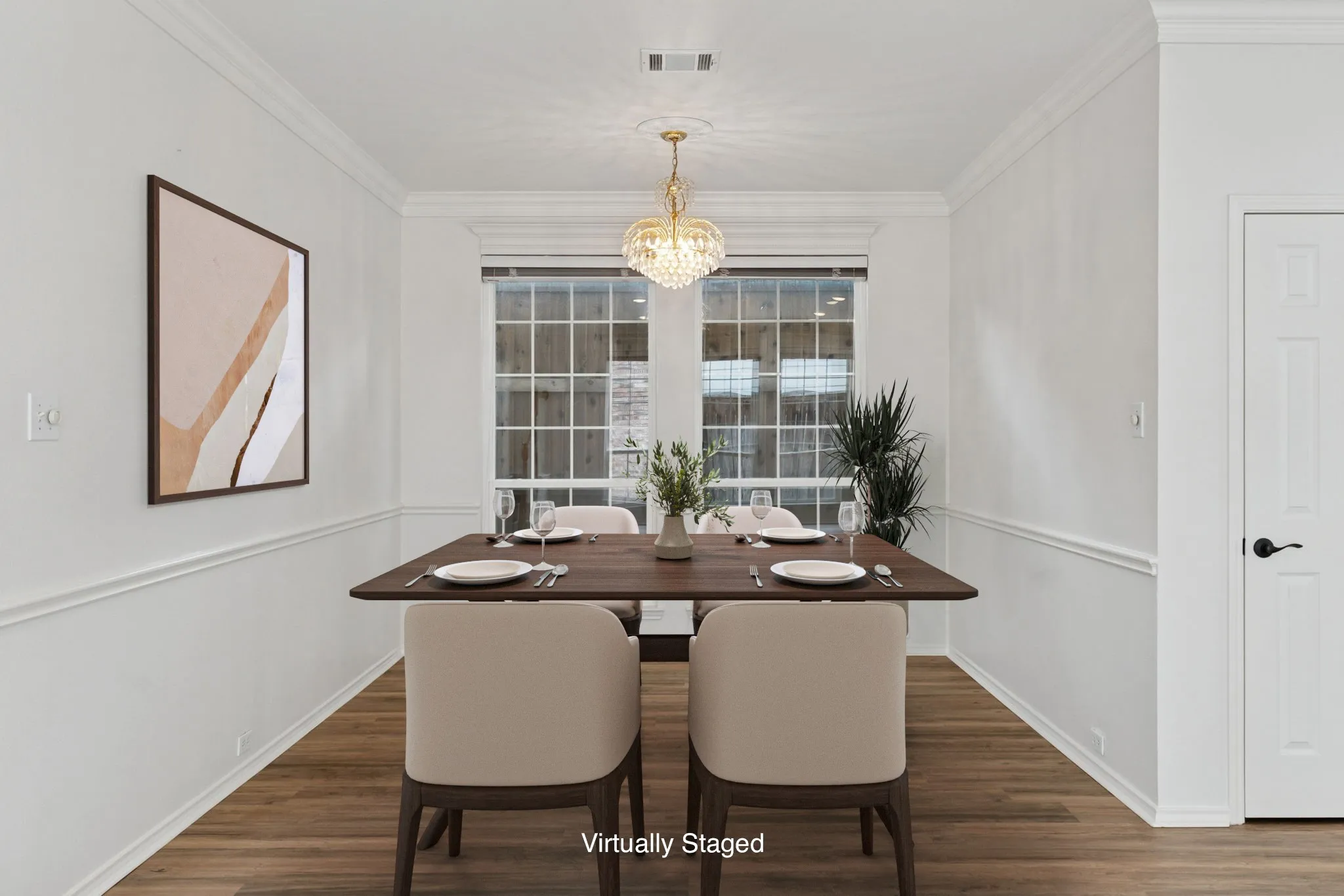 Wood-finish flooring, white walls with decorative molding, and a crystal chandelier