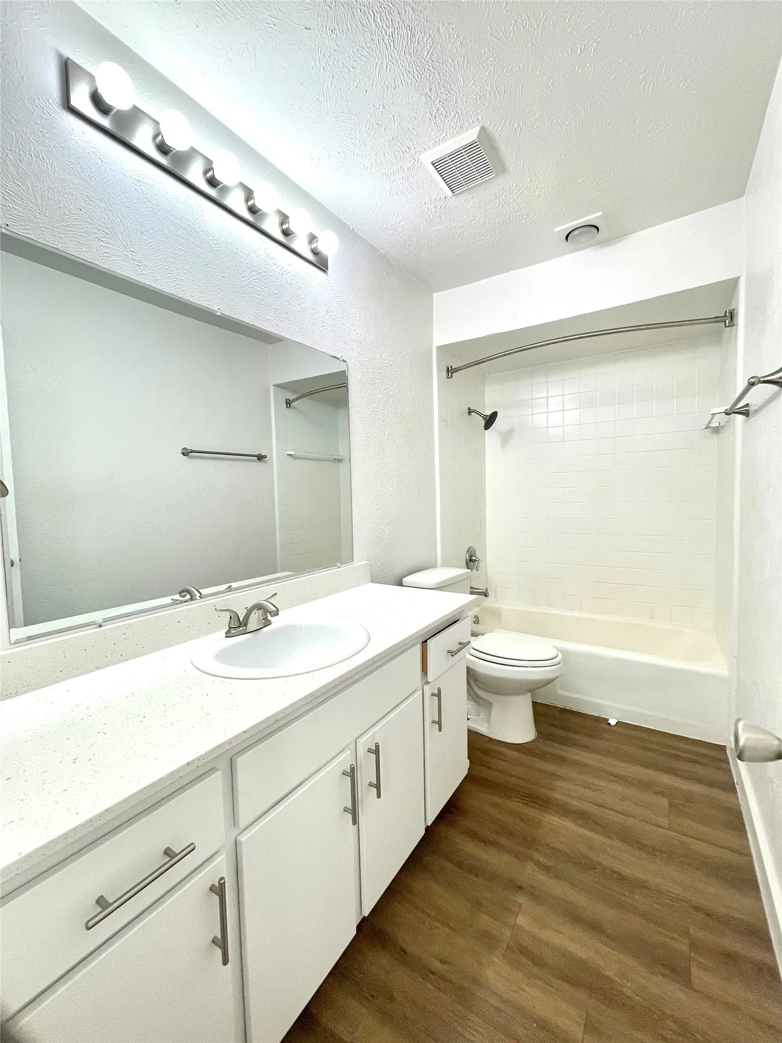 Full bathroom with tiled shower / bath combo, toilet, wood-type flooring, vanity, and a textured ceiling