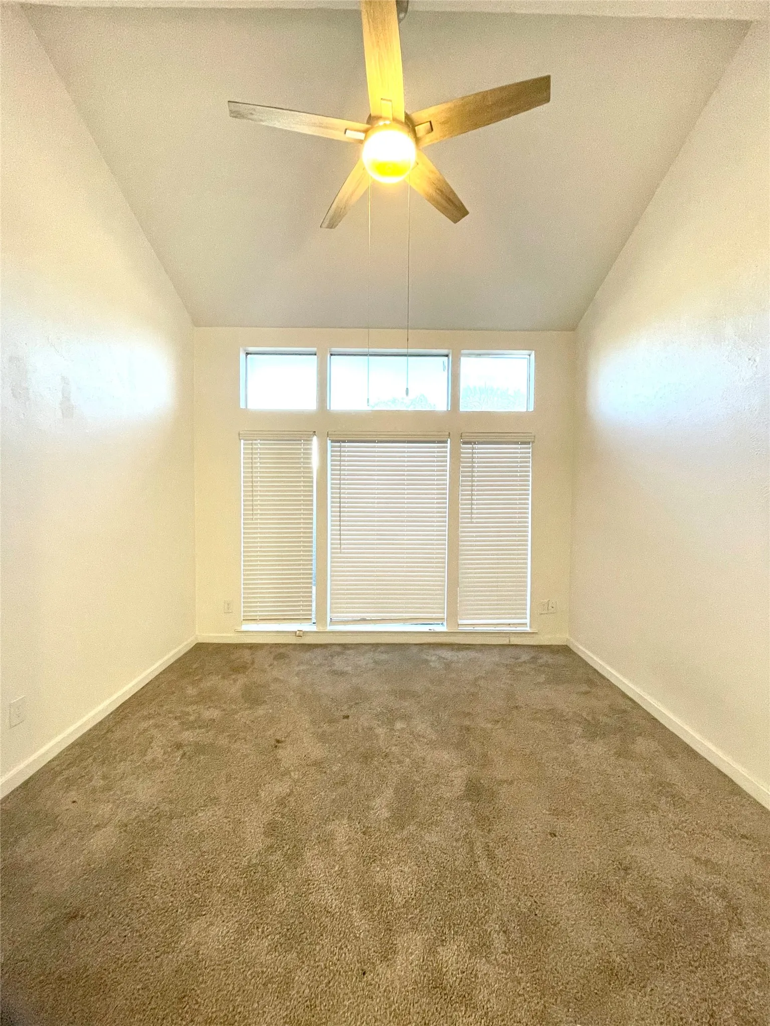 Spare room featuring high vaulted ceiling, dark carpet, and ceiling fan