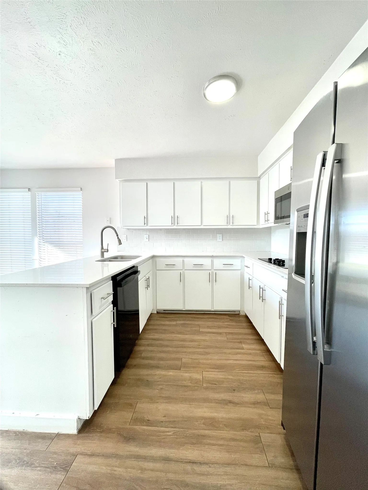 Kitchen with black appliances, light hardwood / wood-style floors, kitchen peninsula, sink, and white cabinetry