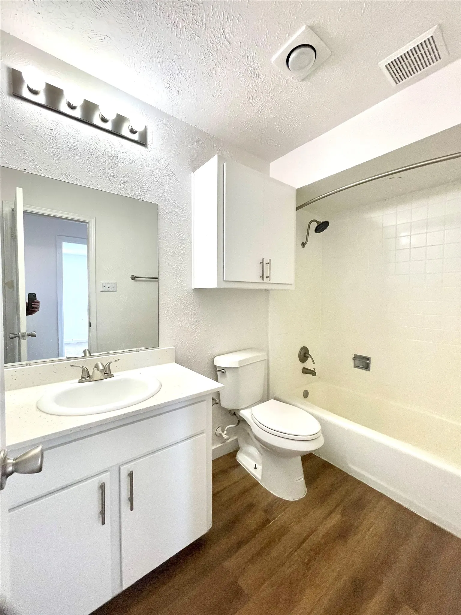Full bathroom with a textured ceiling, bathing tub / shower combination, hardwood / wood-style flooring, toilet, and vanity