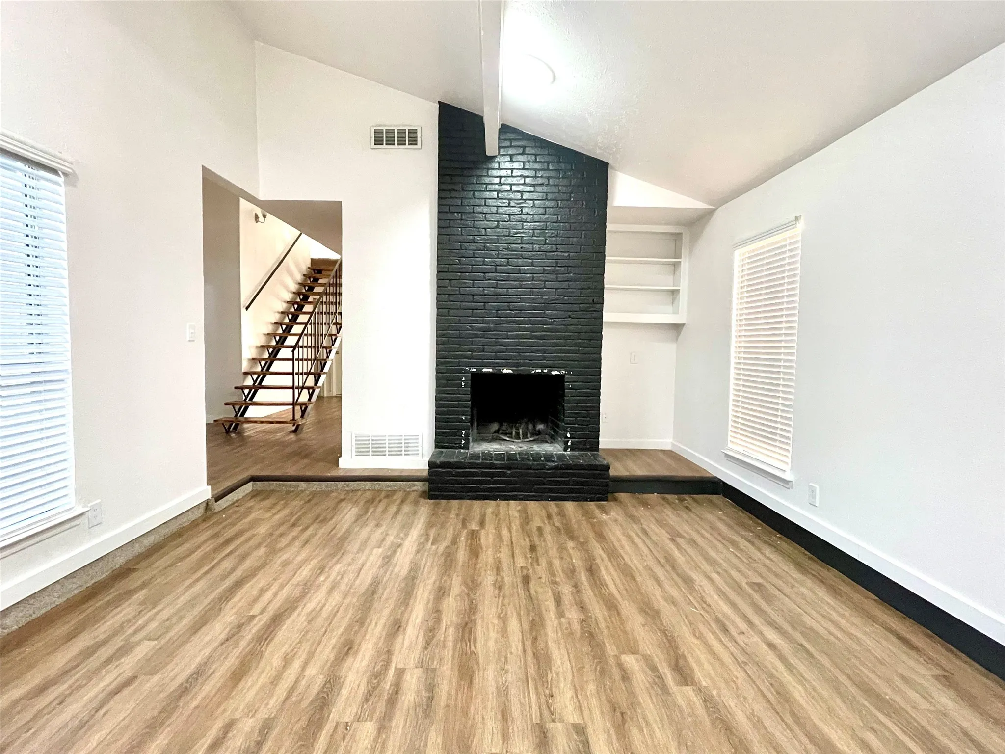 Unfurnished living room featuring lofted ceiling, light hardwood / wood-style floors, a fireplace, and built in shelves