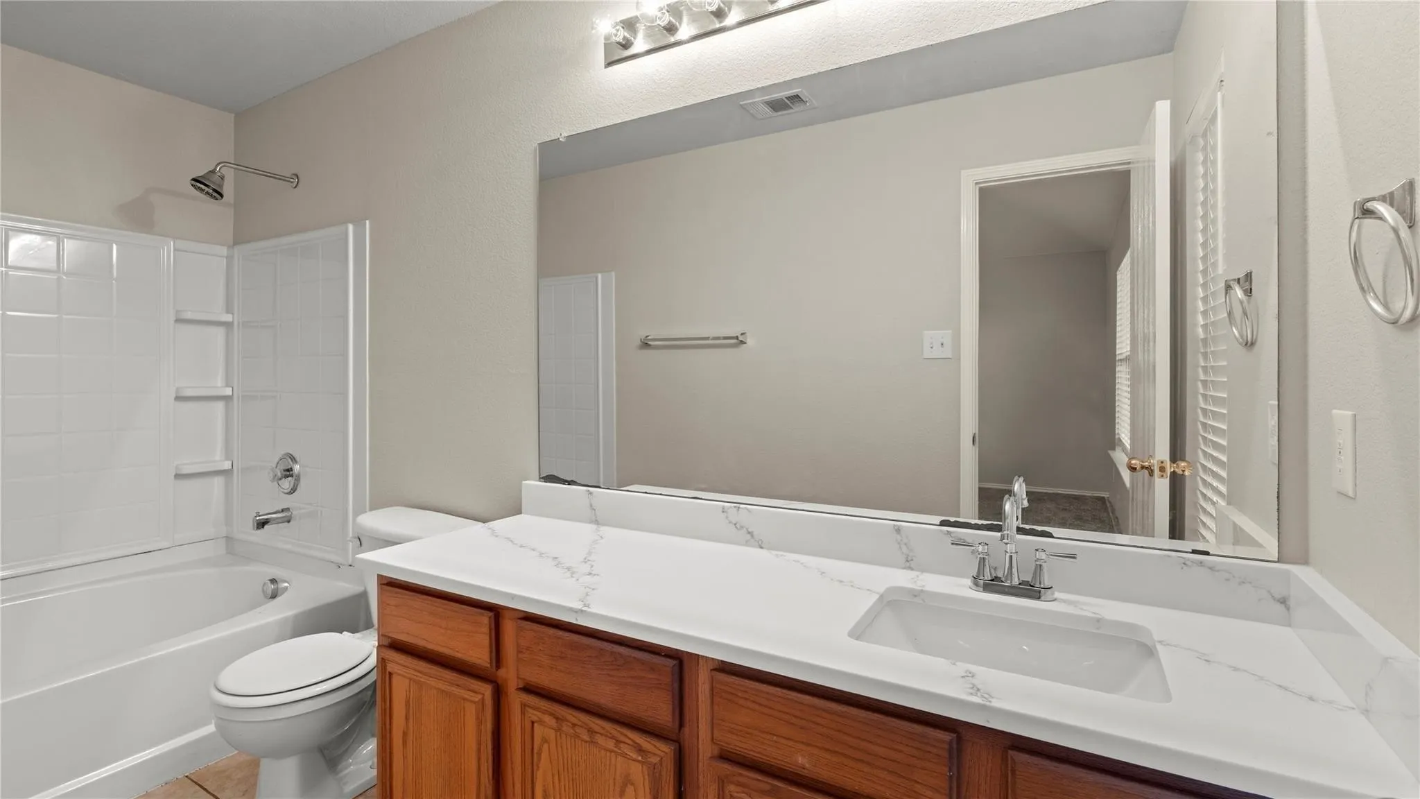 White bathtub and shower combination with tile surround, wood-finish vanity with an integrated sink, white countertop, and an expansive wall mirror