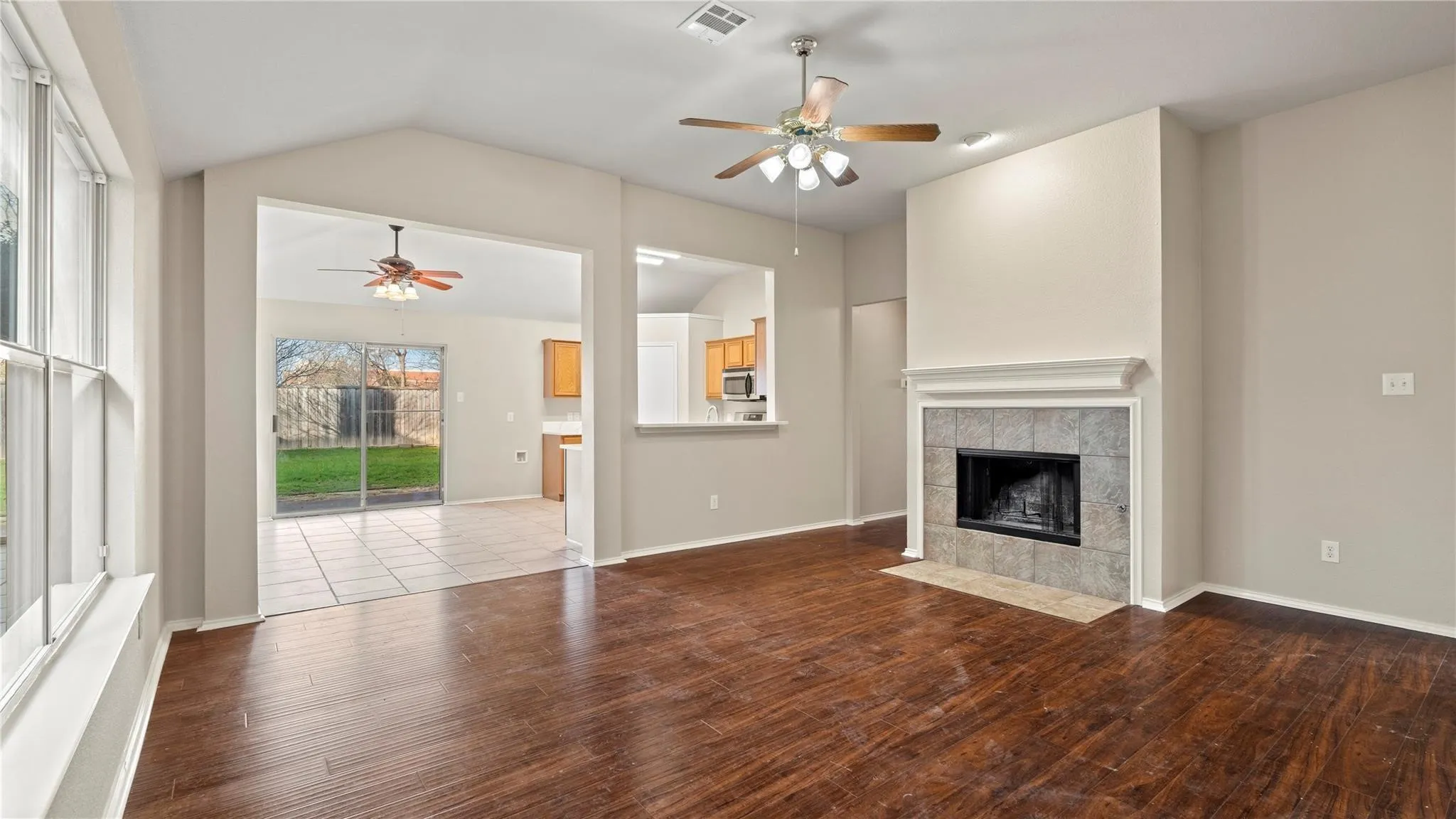 Vaulted ceiling with a ceiling fan, wood-finish flooring, tile-surround fireplace with a mantel, and a sliding glass door