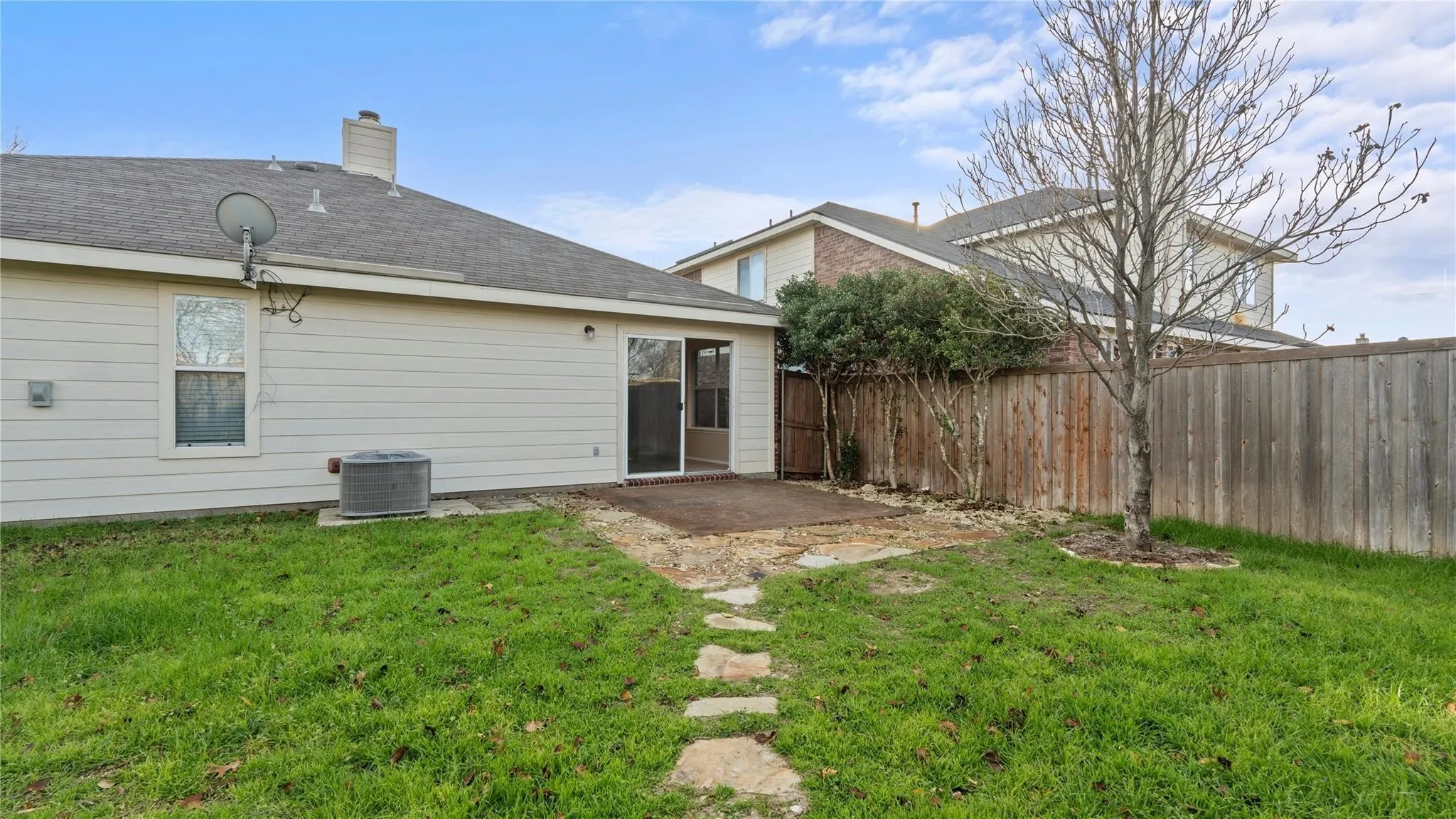 Expansive grass yard featuring a stone pathway, a mature tree, and a wood privacy fence