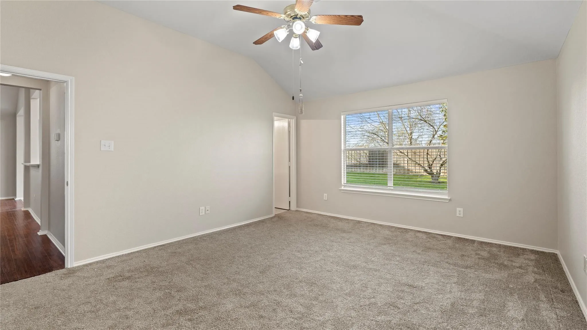 Carpeted room featuring a vaulted ceiling and a wood-finish ceiling fan