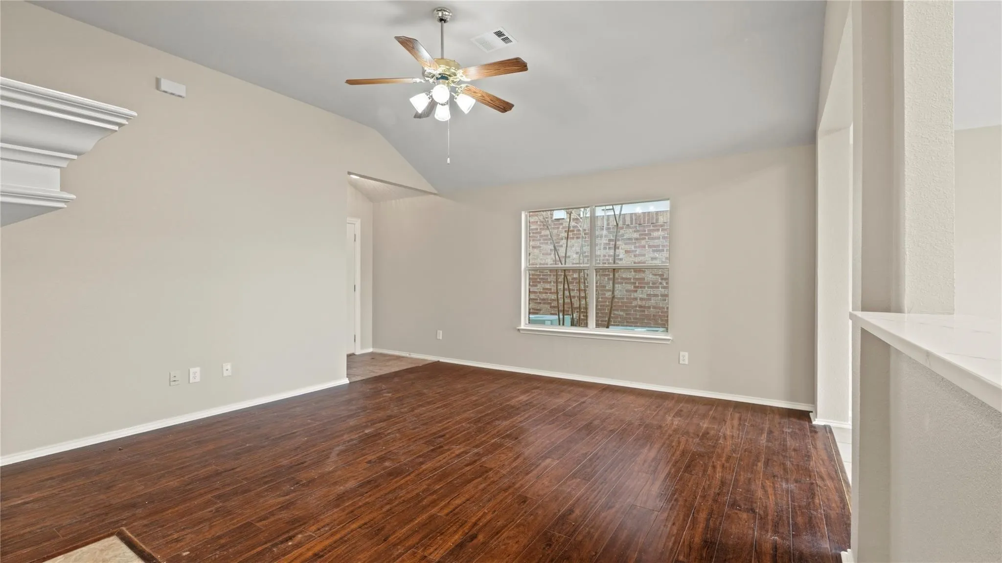 Vaulted ceiling with a ceiling fan, wood-finish flooring, and a window with a brick exterior view