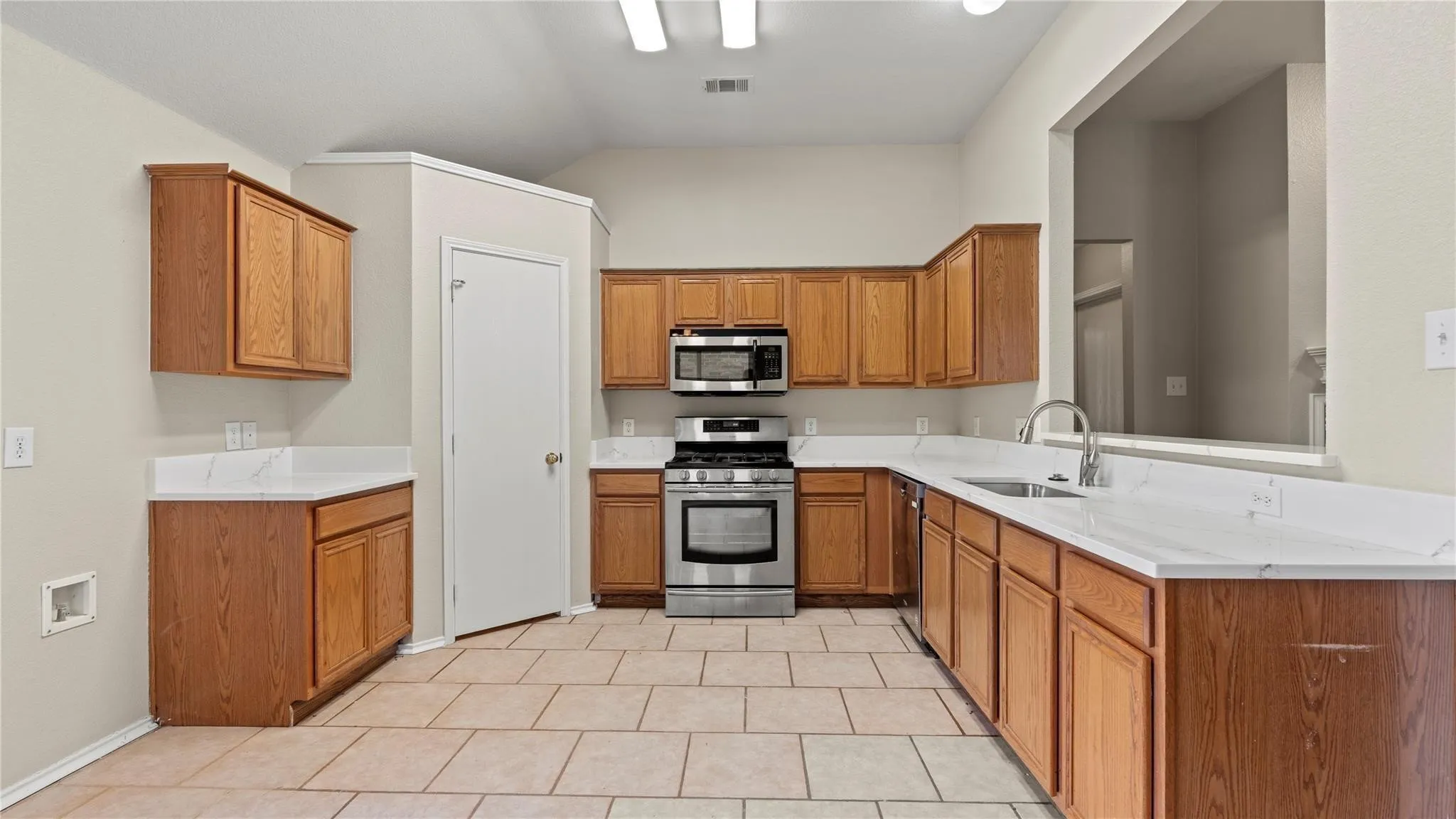 Kitchen featuring stone tile flooring, light wood-finish cabinetry, white countertops, a stainless steel gas range, and a stainless steel microwave