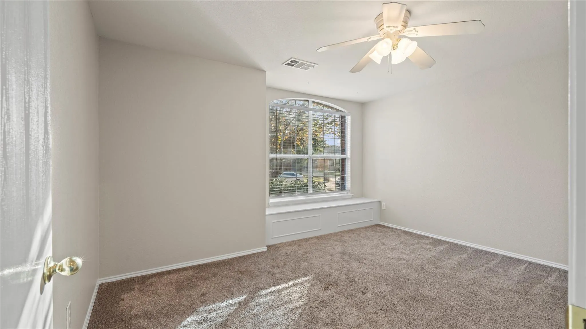 Arched window with a built-in window seat, ceiling fan, and neutral carpet flooring