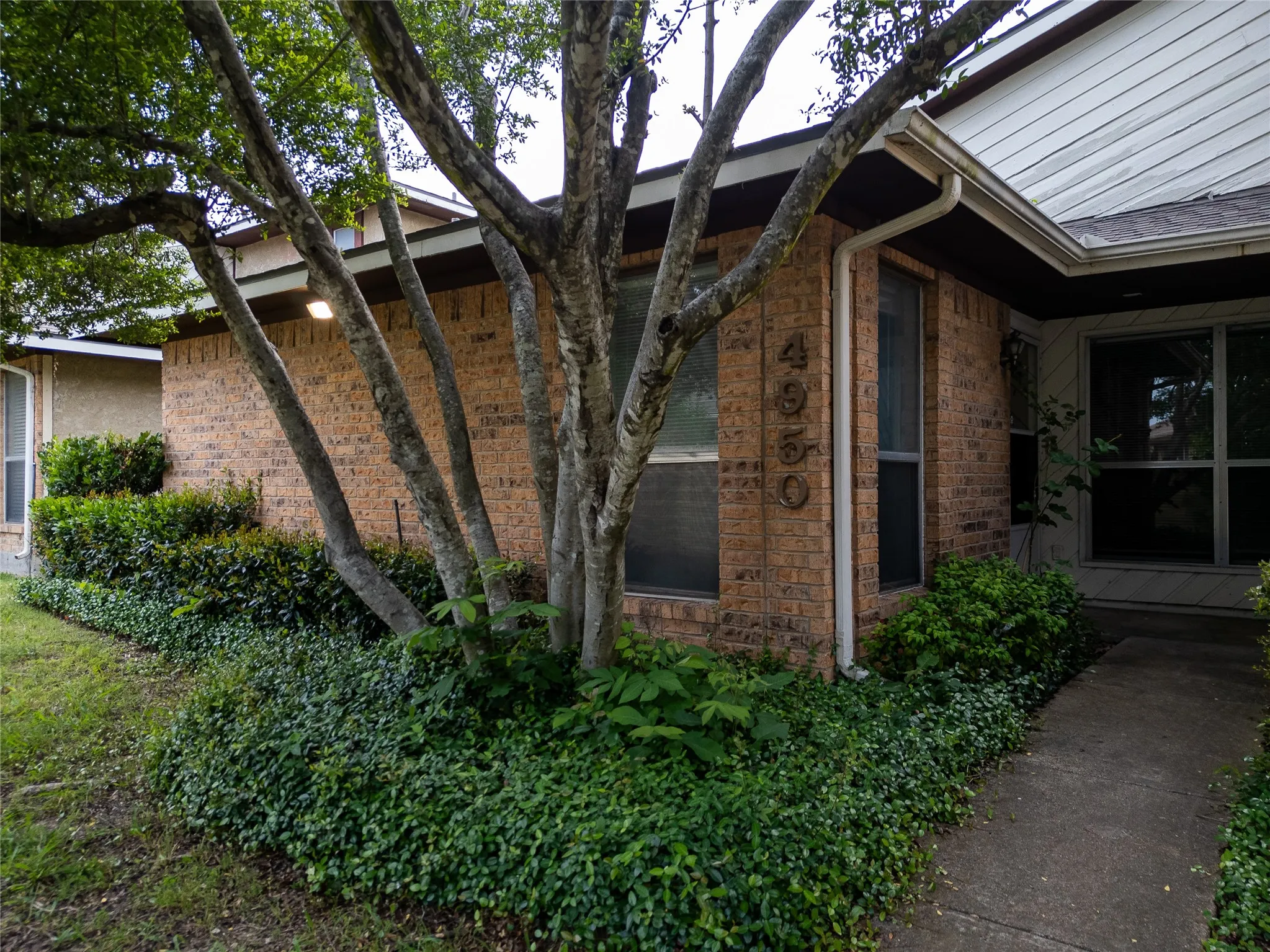 Brick exterior with siding accents, established landscaping, and a concrete pathway