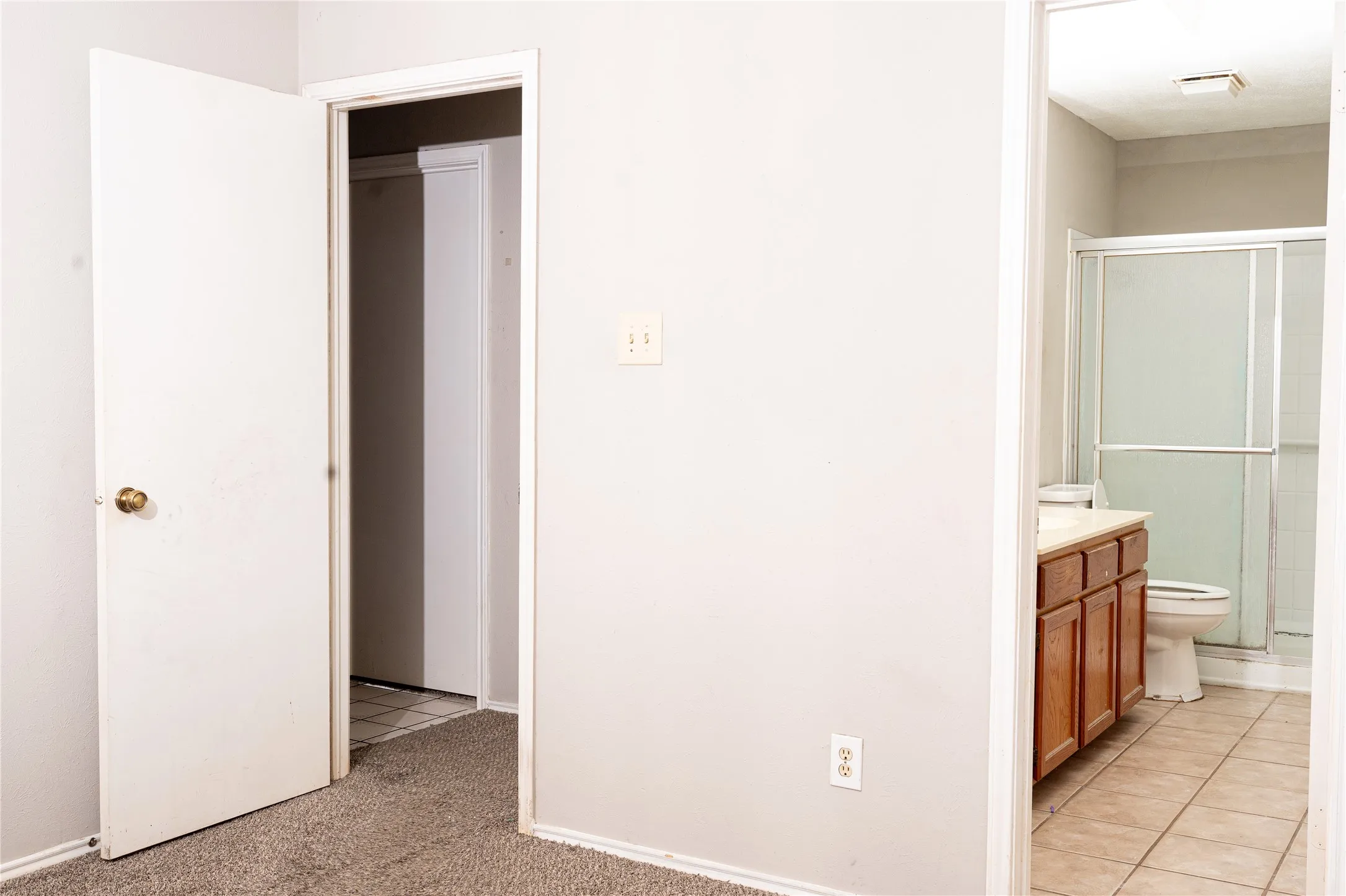 Bathroom featuring a shower with a sliding glass enclosure, a single vanity with wood-finish cabinetry, and tiled flooring