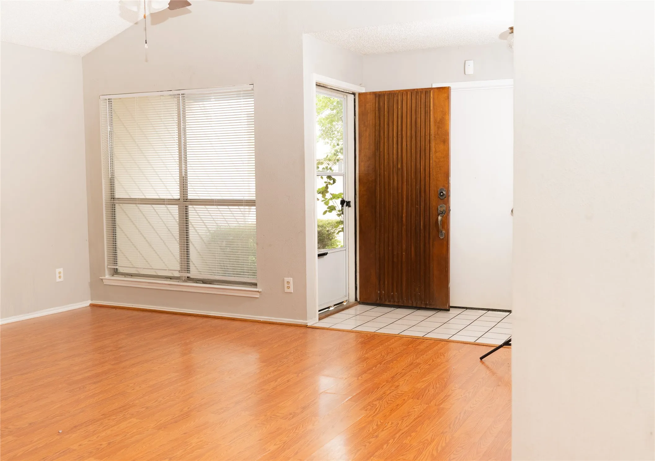 Vaulted ceiling with a ceiling fan, wood-finish flooring, and a large window with blinds