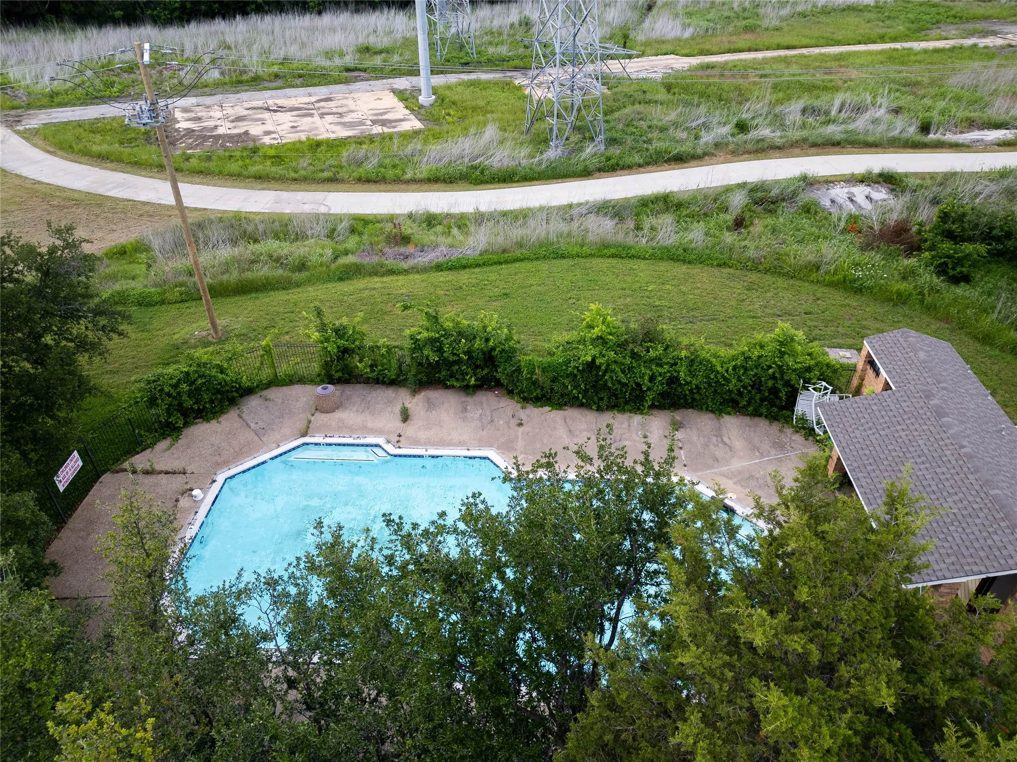 Expansive outdoor pool with integrated steps, concrete surround, and adjacent building with a shingled roof