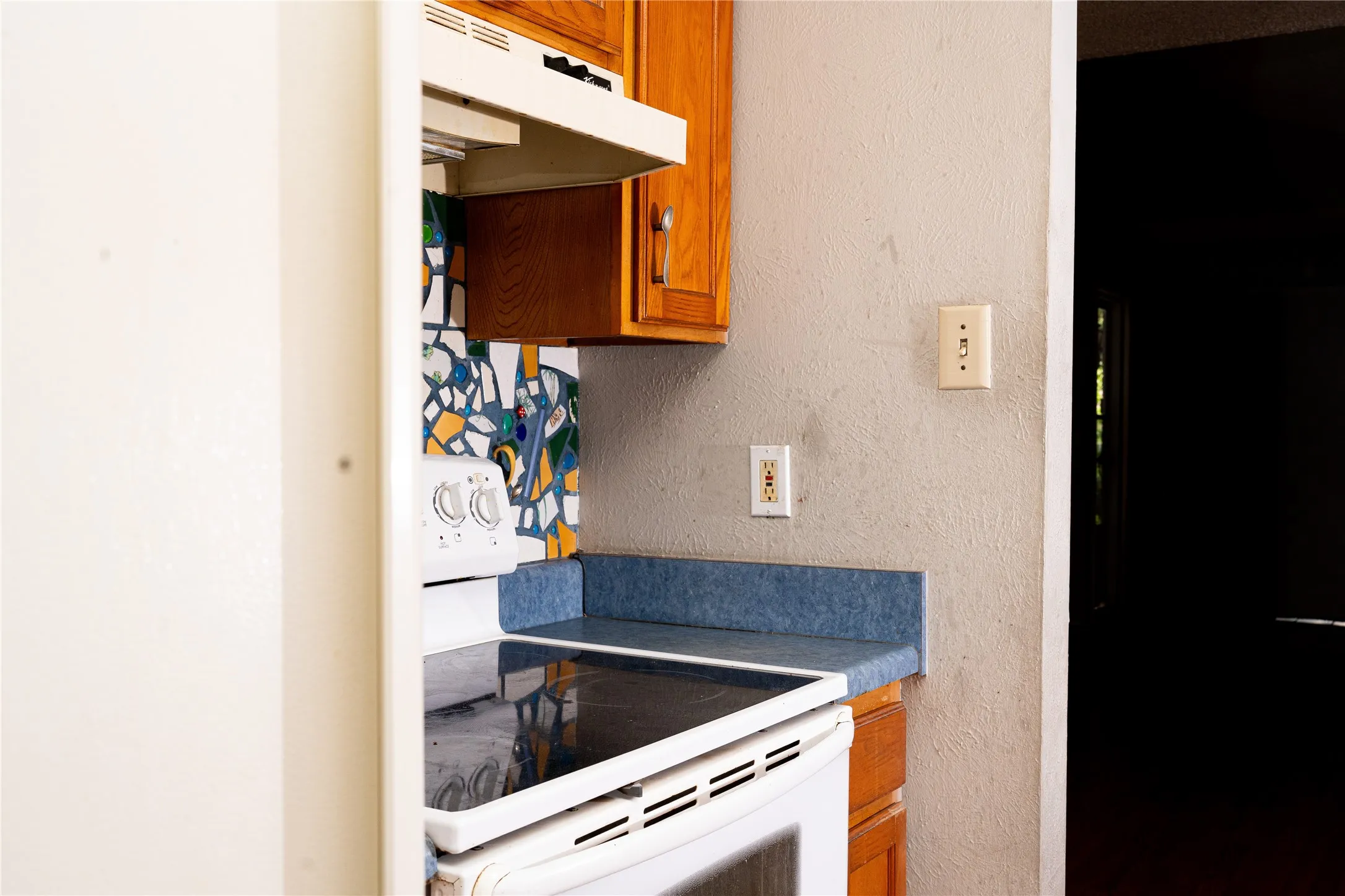 White electric range, mosaic tile backsplash, wood cabinets, and blue countertop