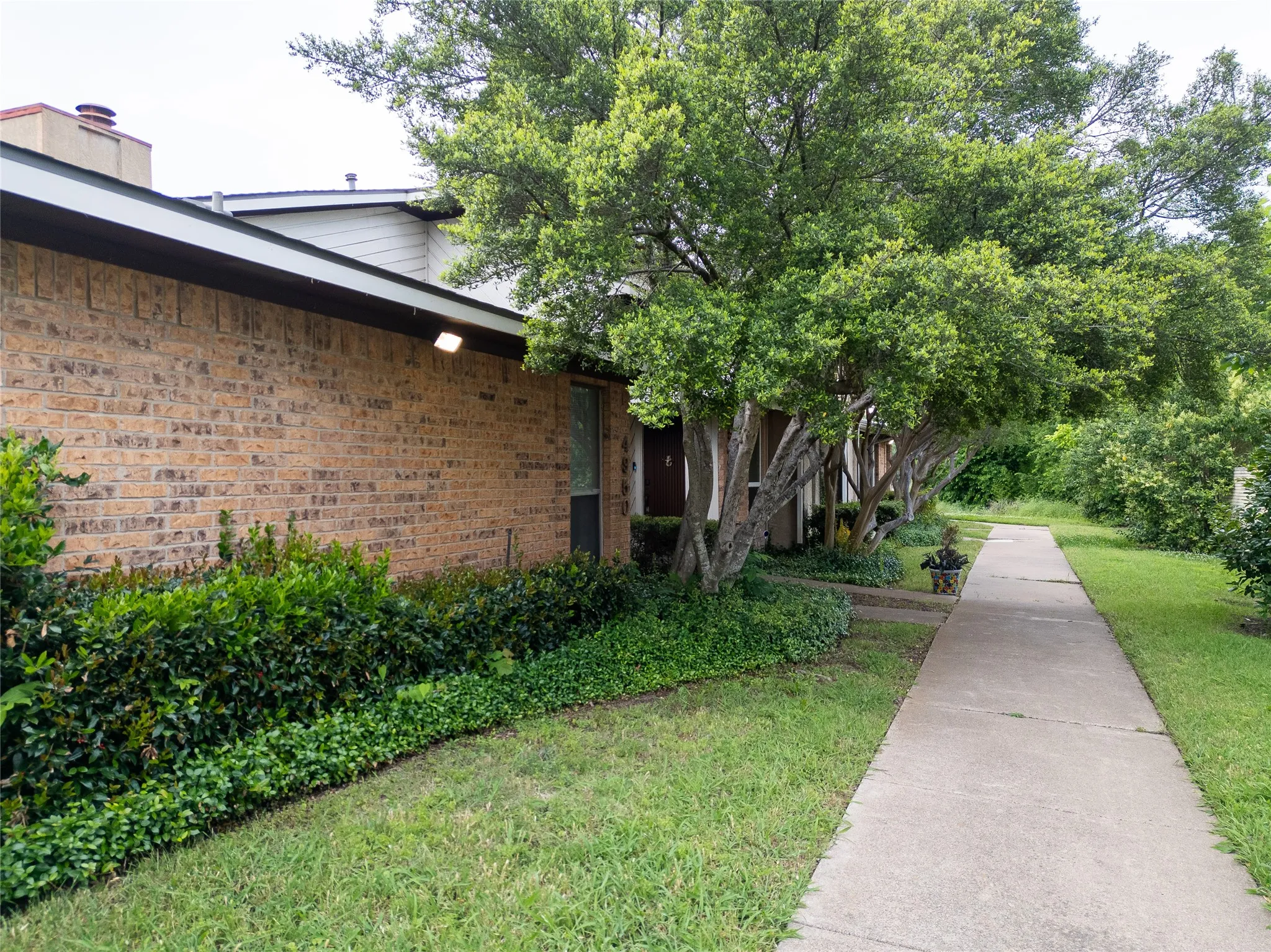 Brick exterior, mature trees, concrete walkway, landscaped shrubbery, ground cover