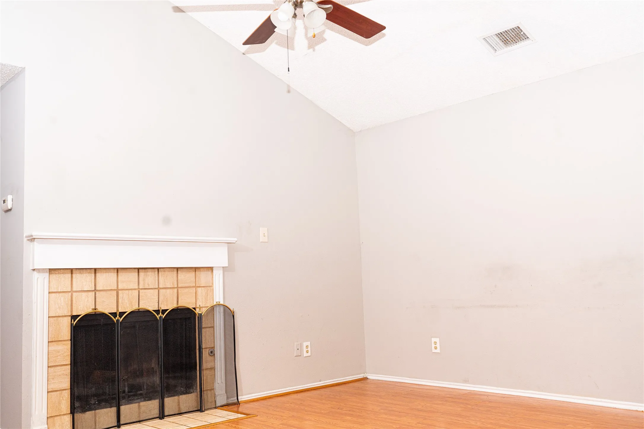 Vaulted ceiling with a ceiling fan, fireplace featuring a tiled surround and mantel, and wood-finish flooring