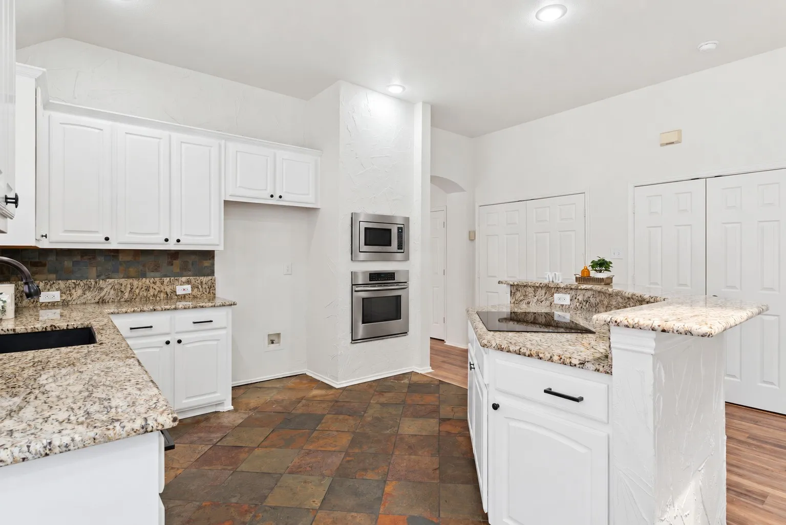 Kitchen featuring granite countertops, white cabinetry with dark hardware, stainless steel built-in appliances, and multi-toned tile flooring