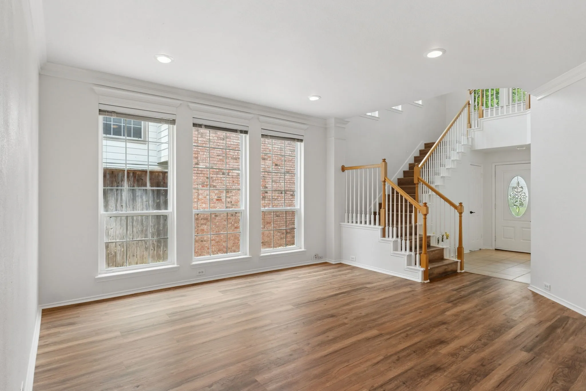 Wood-finish flooring, recessed lighting, white wall paint, three large windows, and a staircase with wood handrails