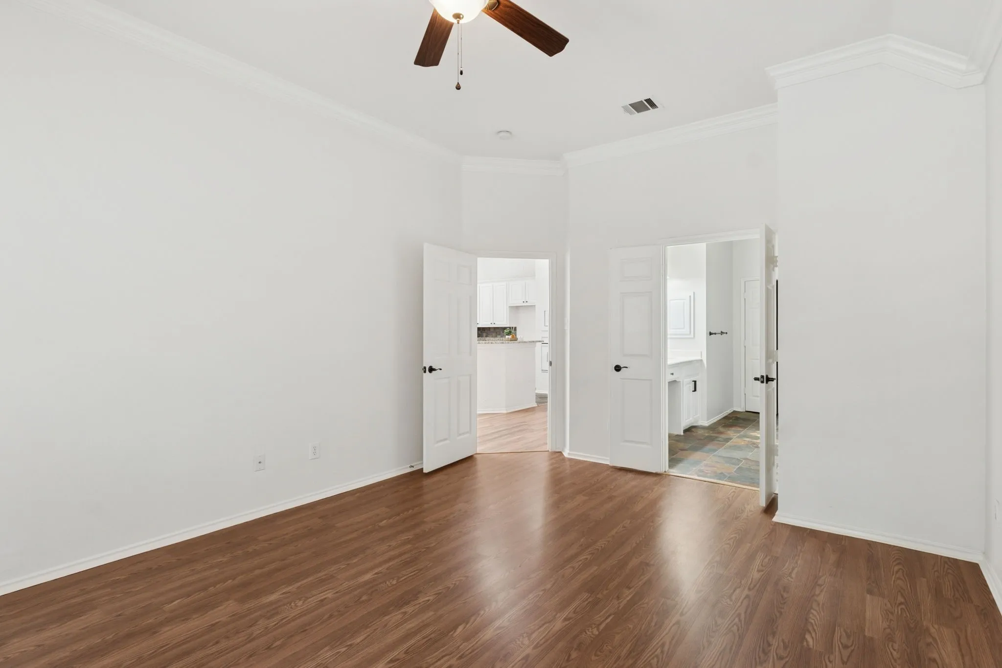 Wood-finish flooring, crown molding, ceiling fan, and white paneled doors