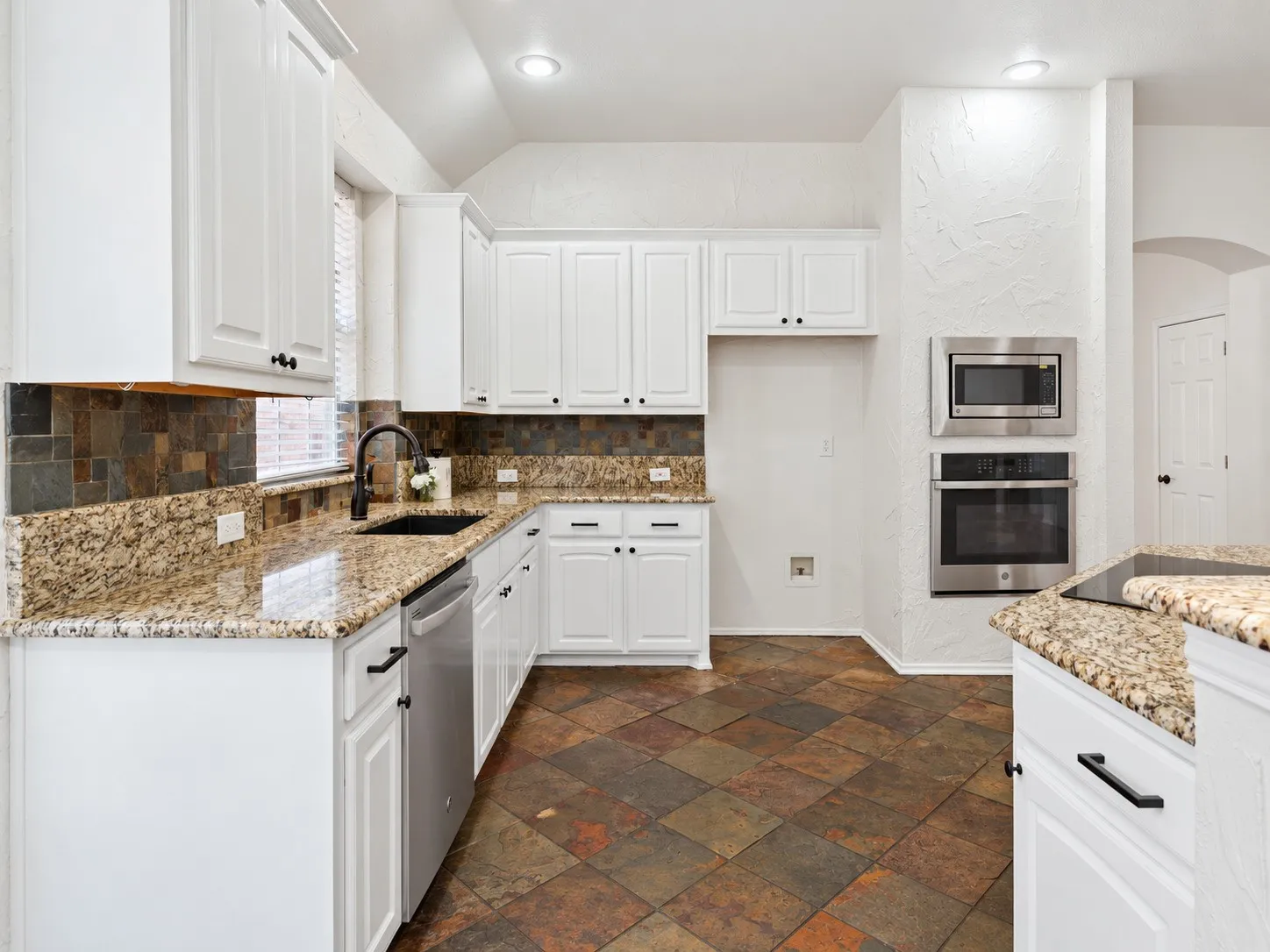 White cabinetry, built-in stainless steel oven and microwave, dark bronze hardware, multi-toned tile flooring, and granite countertops