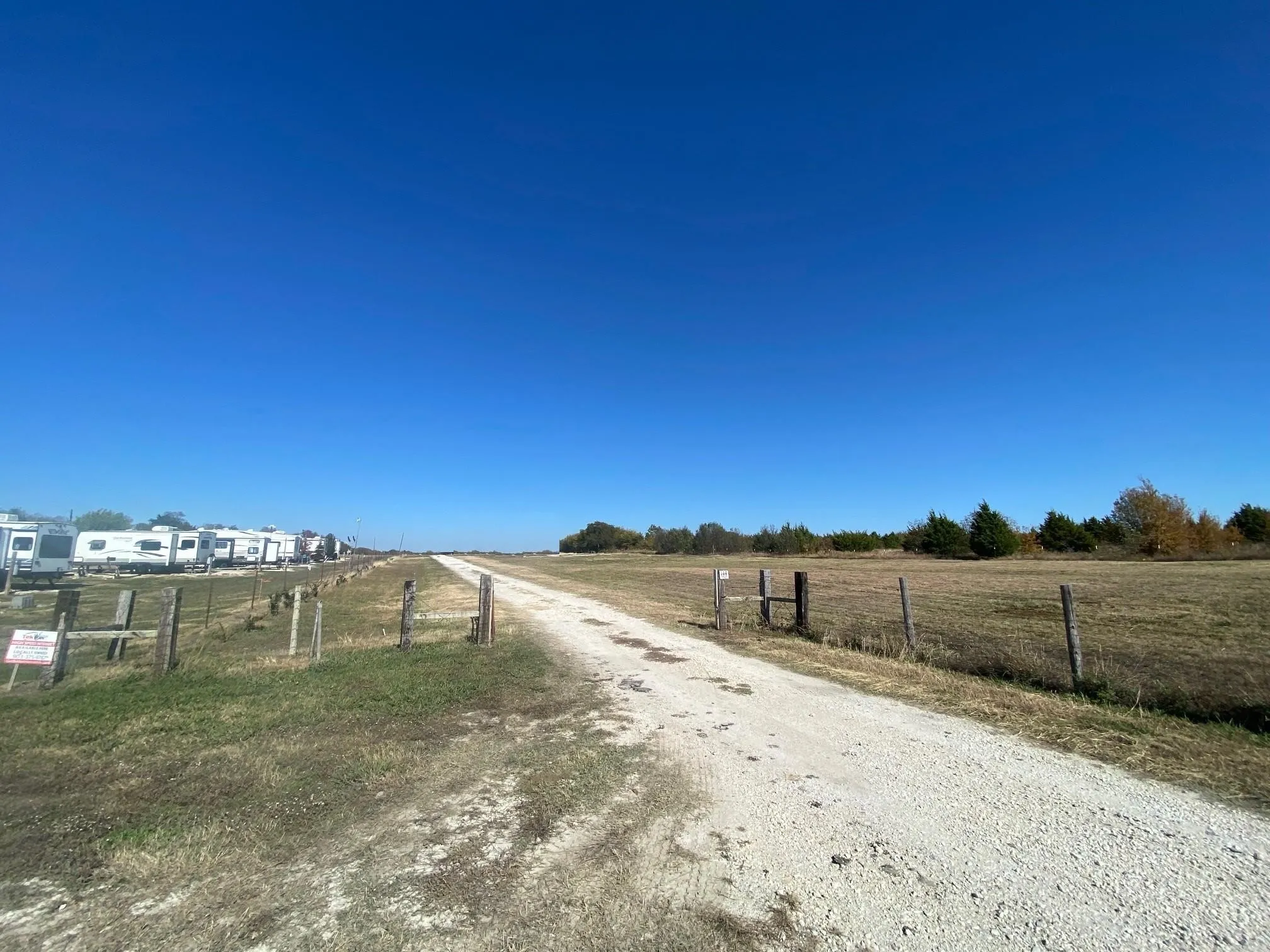 Gravel pathway with a rustic wire fence, expansive open field, and distant trees