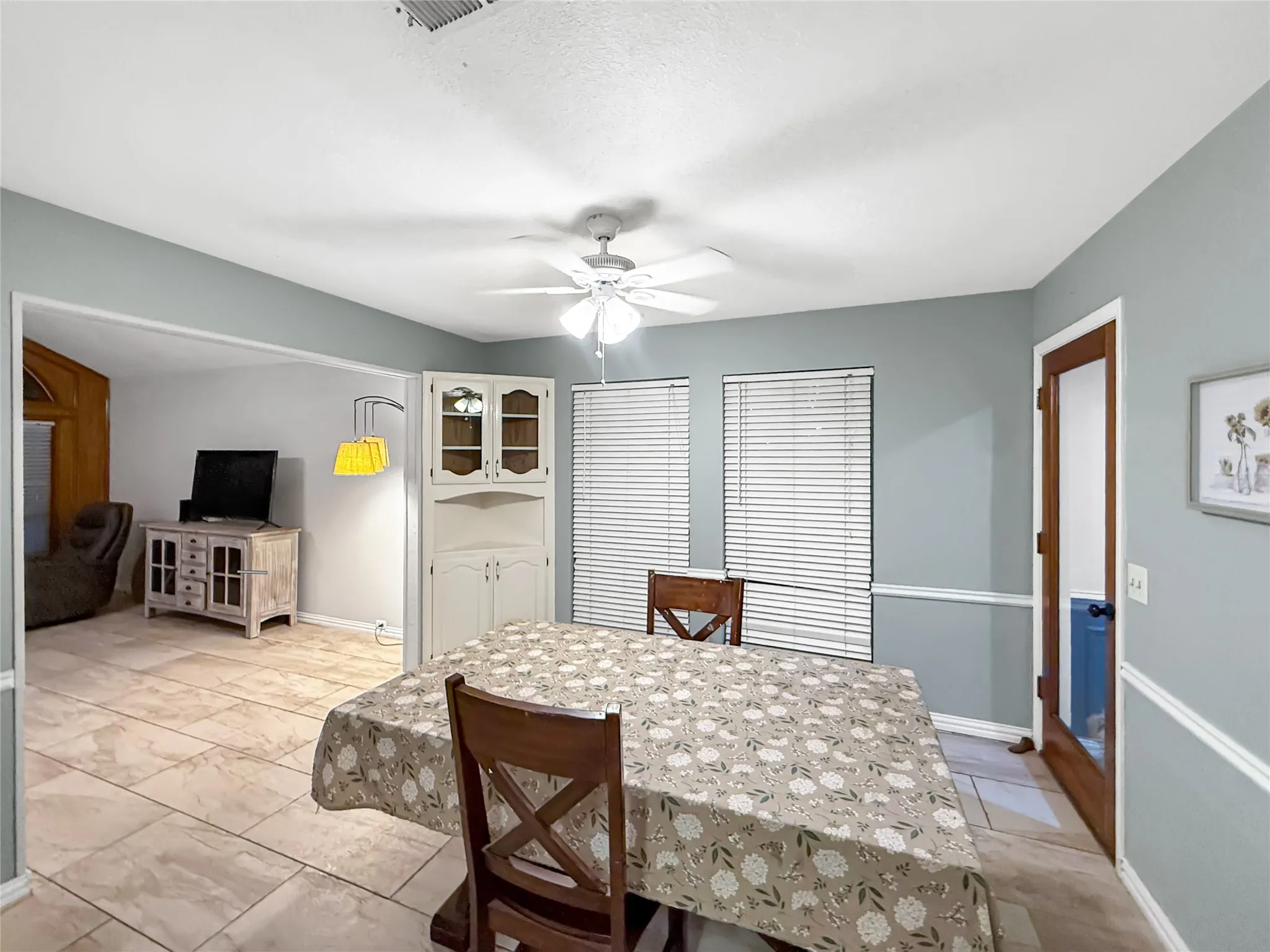 Tile flooring throughout, white ceiling fan with integrated lighting, built-in display cabinetry, and multiple windows with blinds