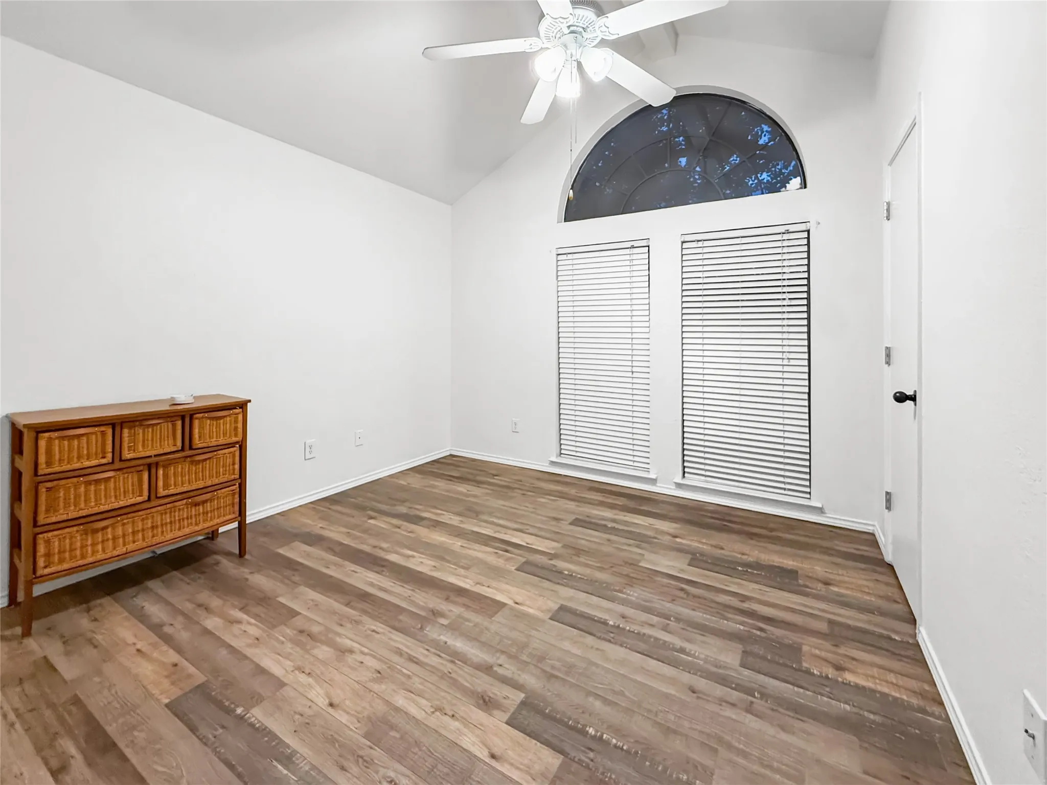 Vaulted ceiling with a white ceiling fan, wood-finish flooring, and white walls