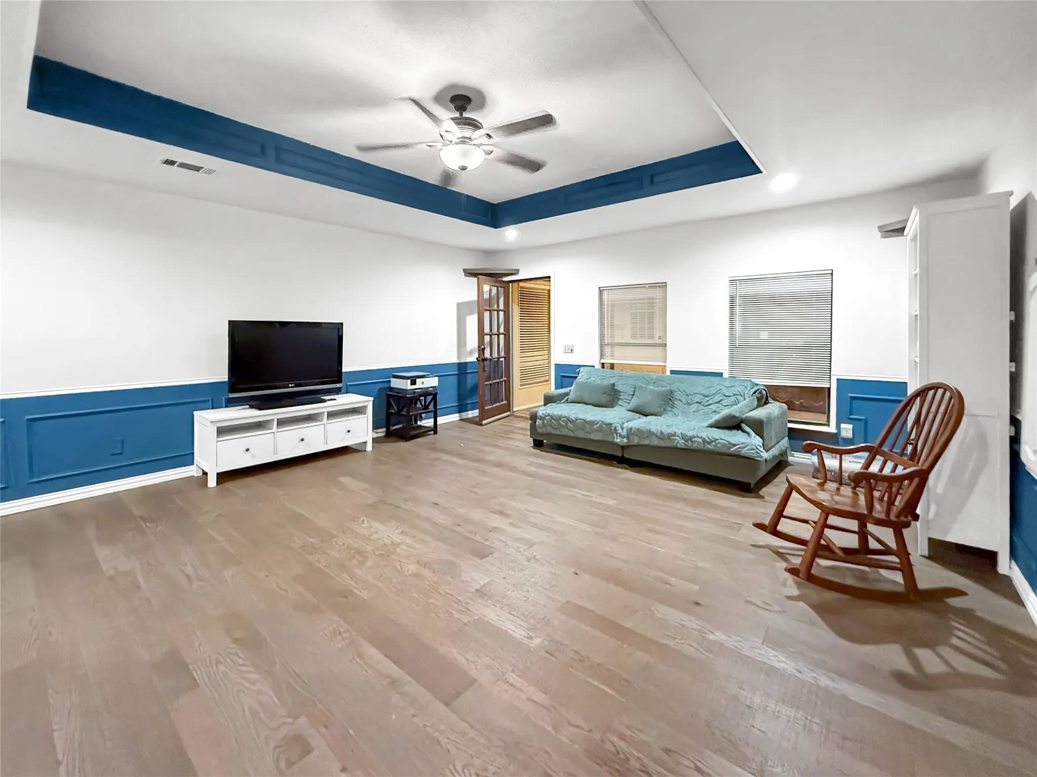 Wood-finish flooring, accent wainscoting, tray ceiling with lighting, ceiling fan, and French doors