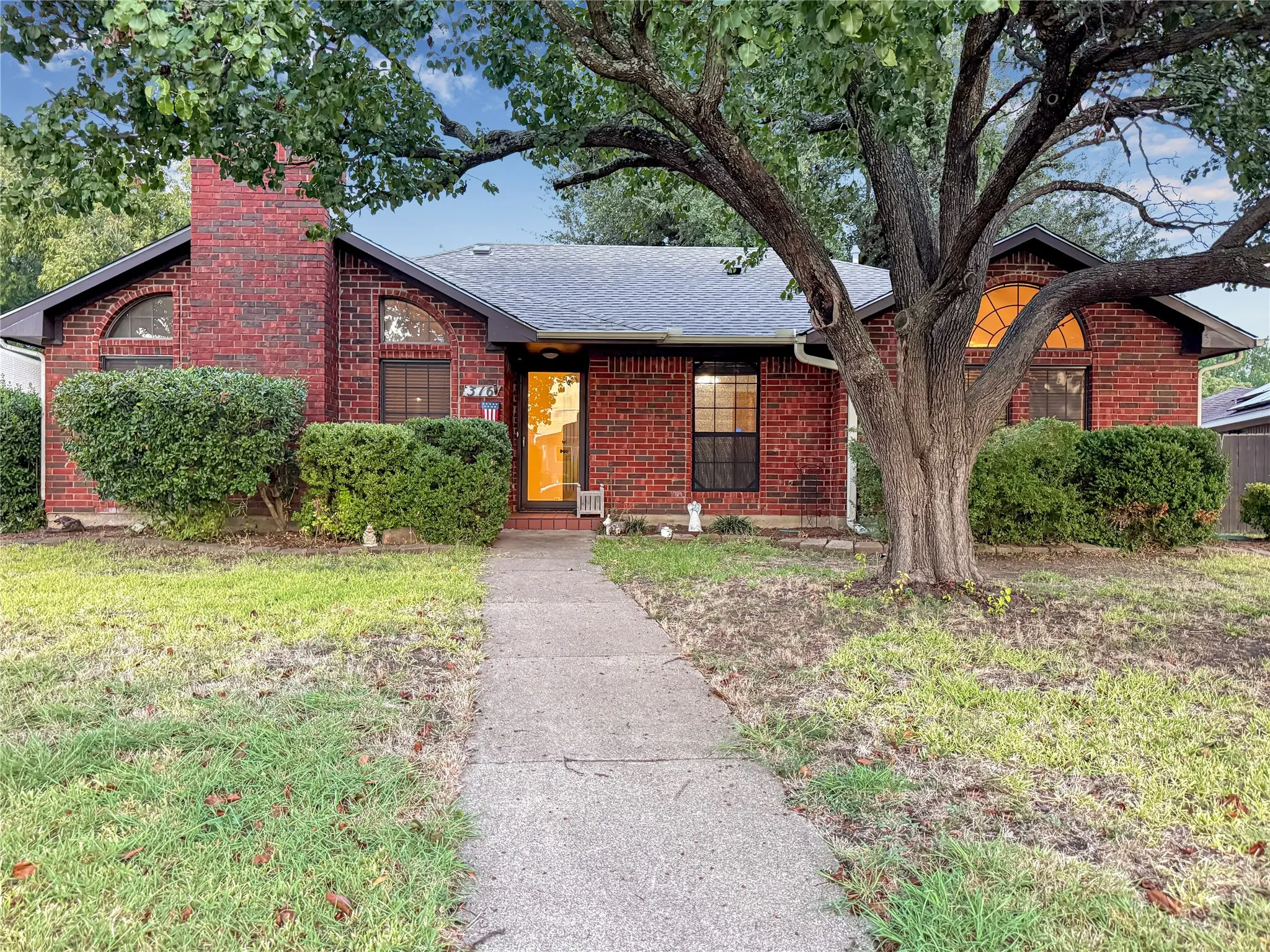 Red brick exterior with a prominent chimney, arched windows, and a mature front yard tree