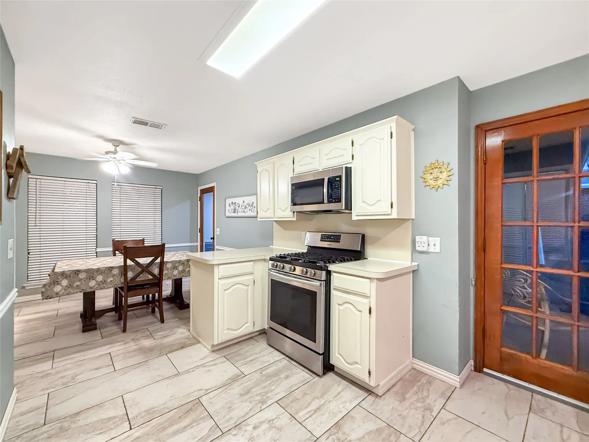 Tile flooring, white cabinetry, stainless steel range, stainless steel microwave, and a wood-frame glass panel door