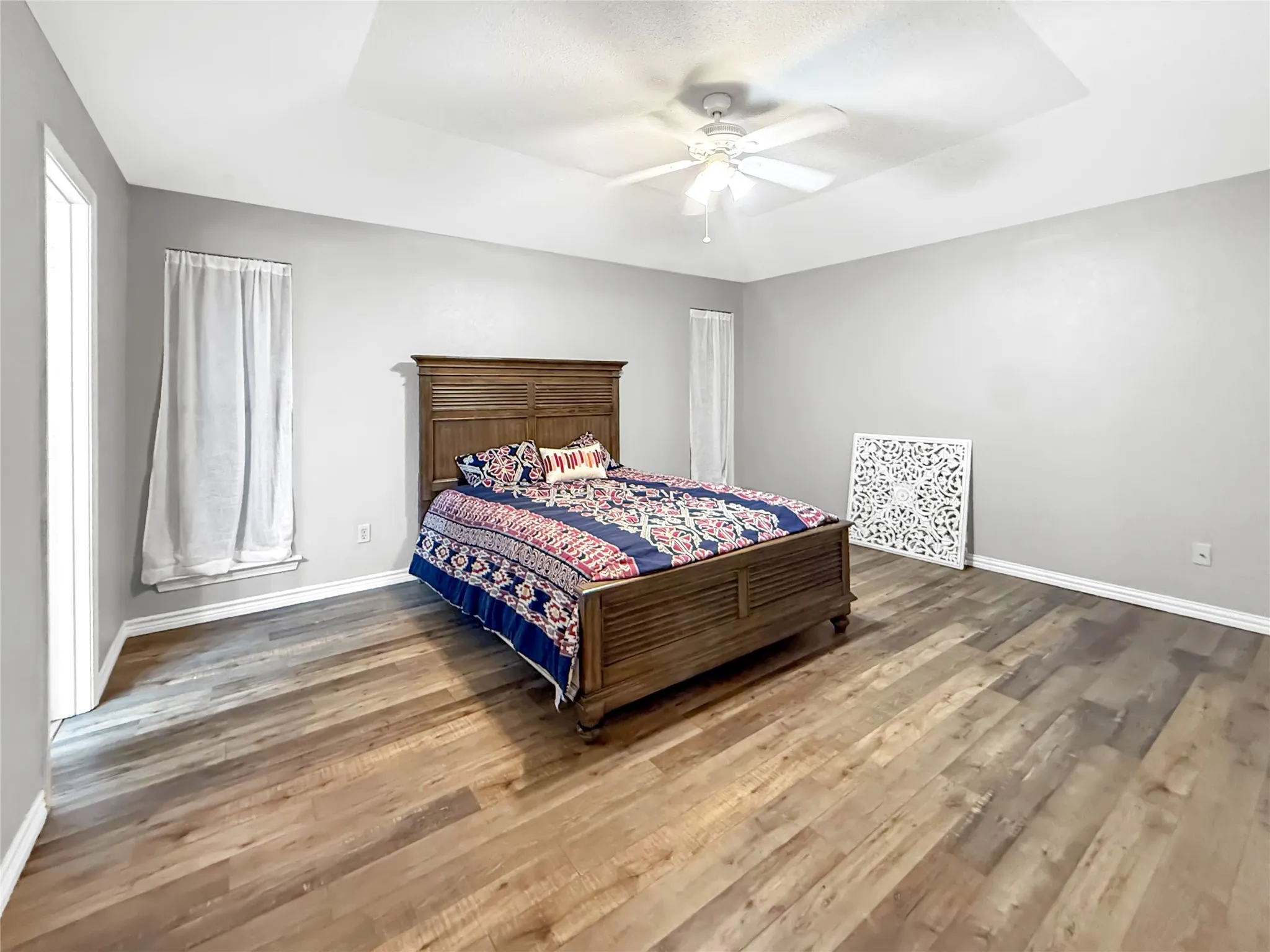 Tray ceiling with a ceiling fan, wood-finish flooring, and light gray walls