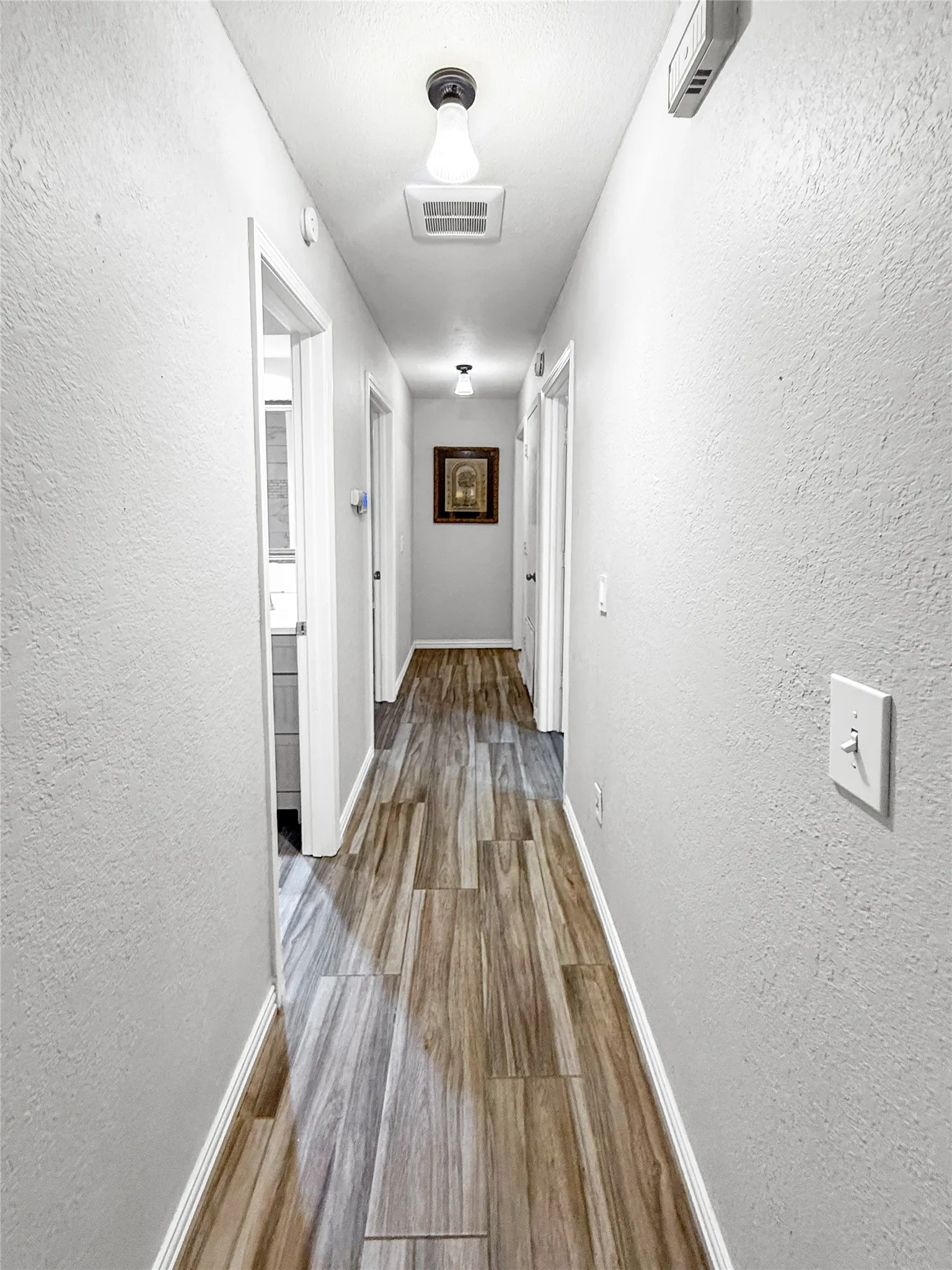 Long hallway featuring wood-finish tile flooring, recessed lighting, and crisp white trim