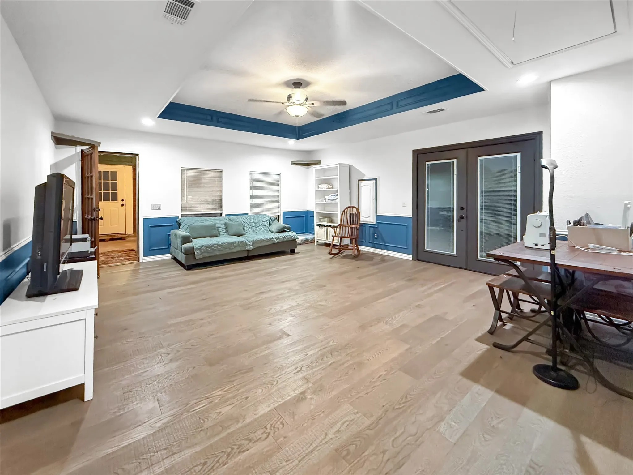 Spacious living area featuring wood-finish flooring, a tray ceiling with a ceiling fan, and French doors