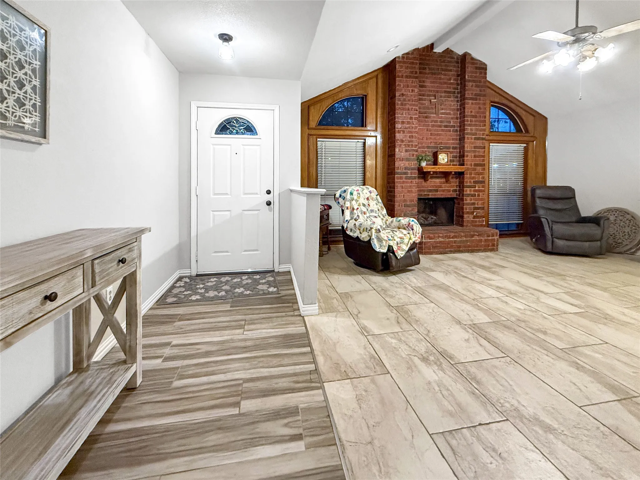 Expansive living space featuring wood-finish flooring, a brick fireplace with a mantel, and vaulted ceilings