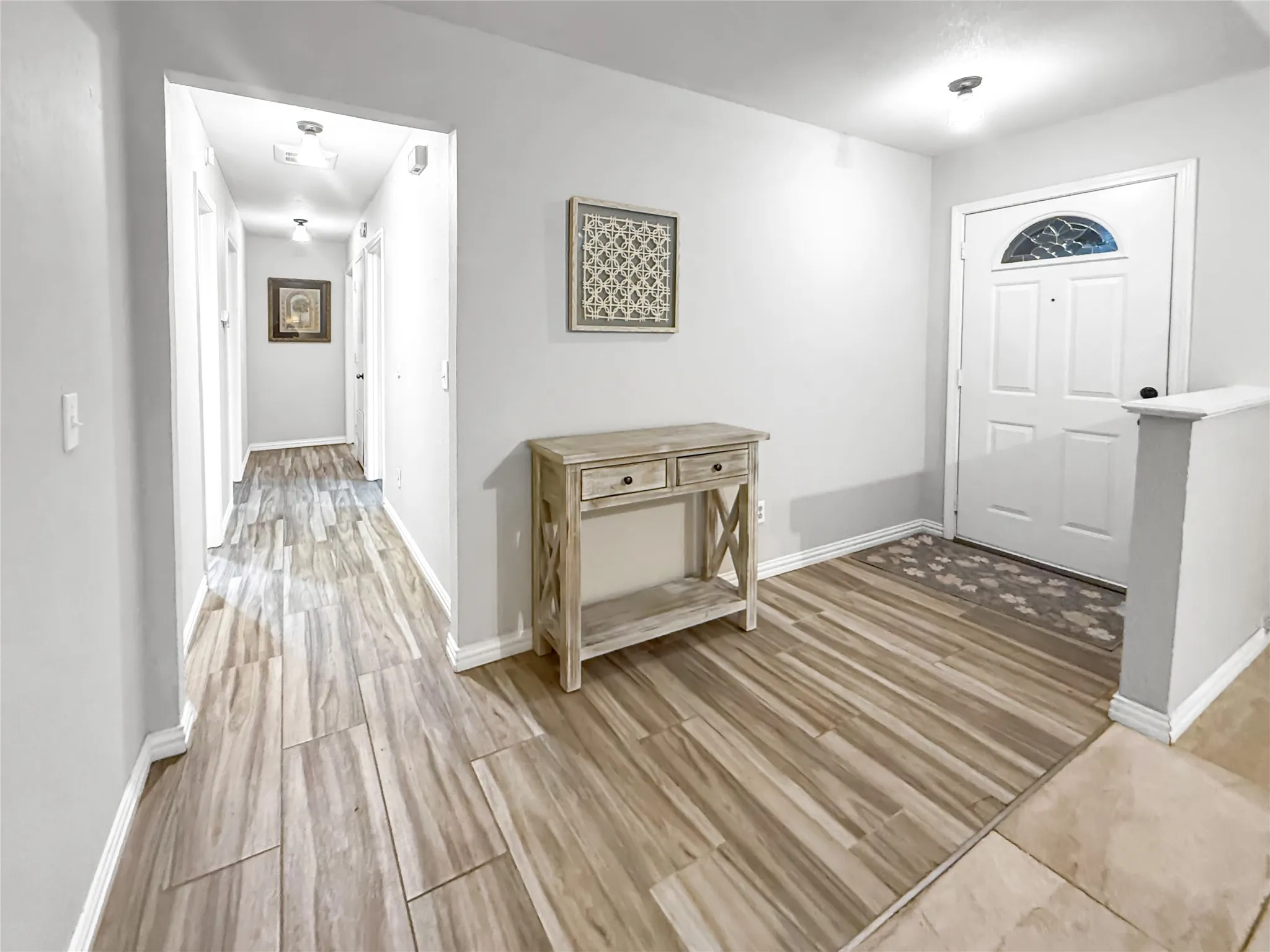 Wood-finish flooring throughout, bright white entry door with decorative glass, and a neutral wall color