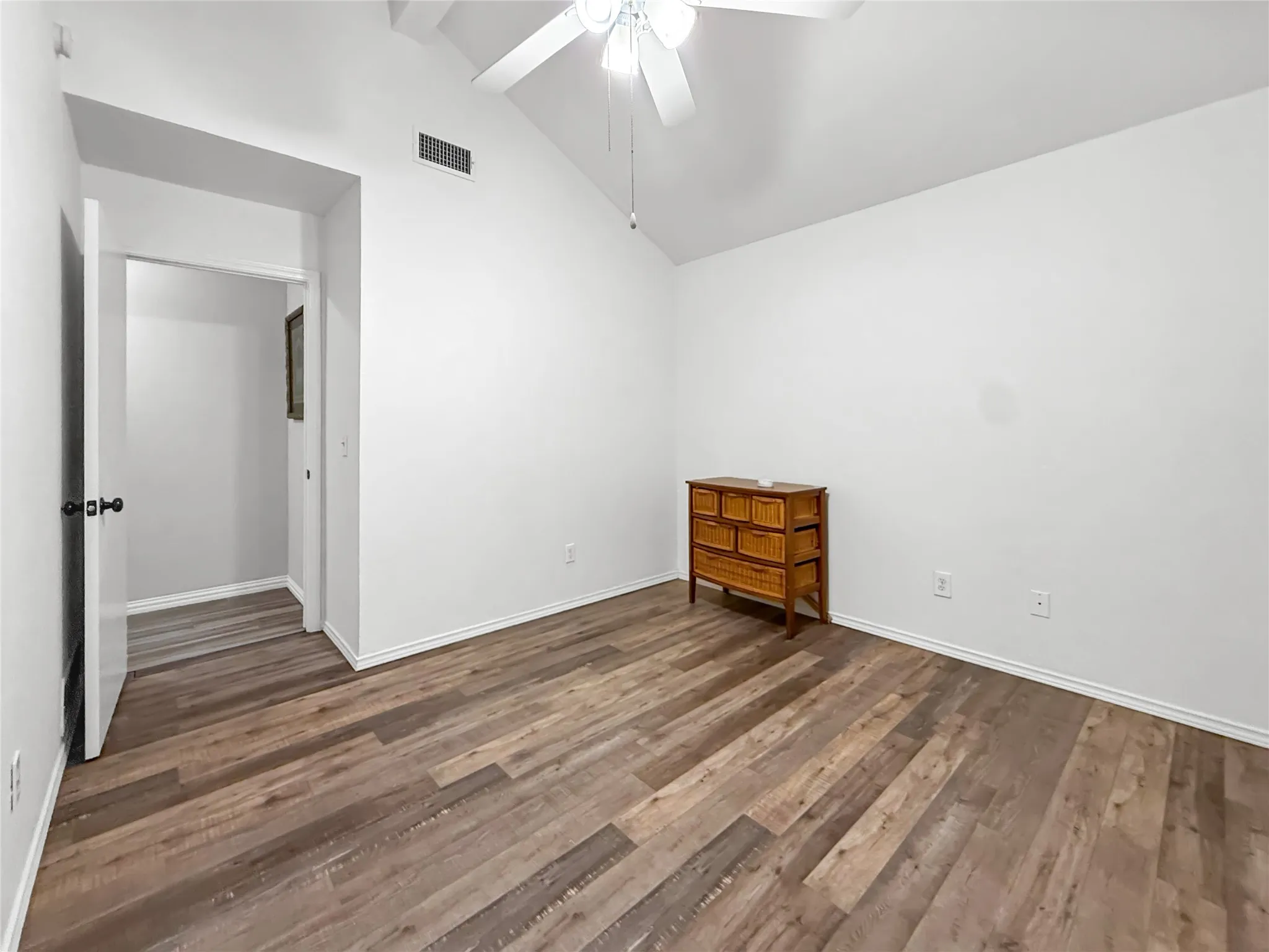 Vaulted ceiling with a white ceiling fan, wood-finish flooring, and white walls