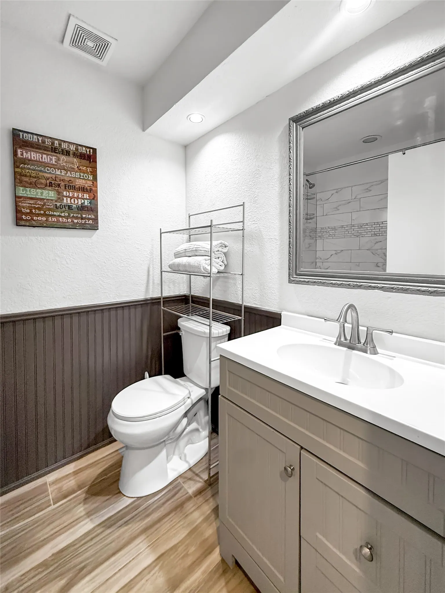 White single-basin vanity with a light countertop, wood-finish flooring, and dark wainscoting