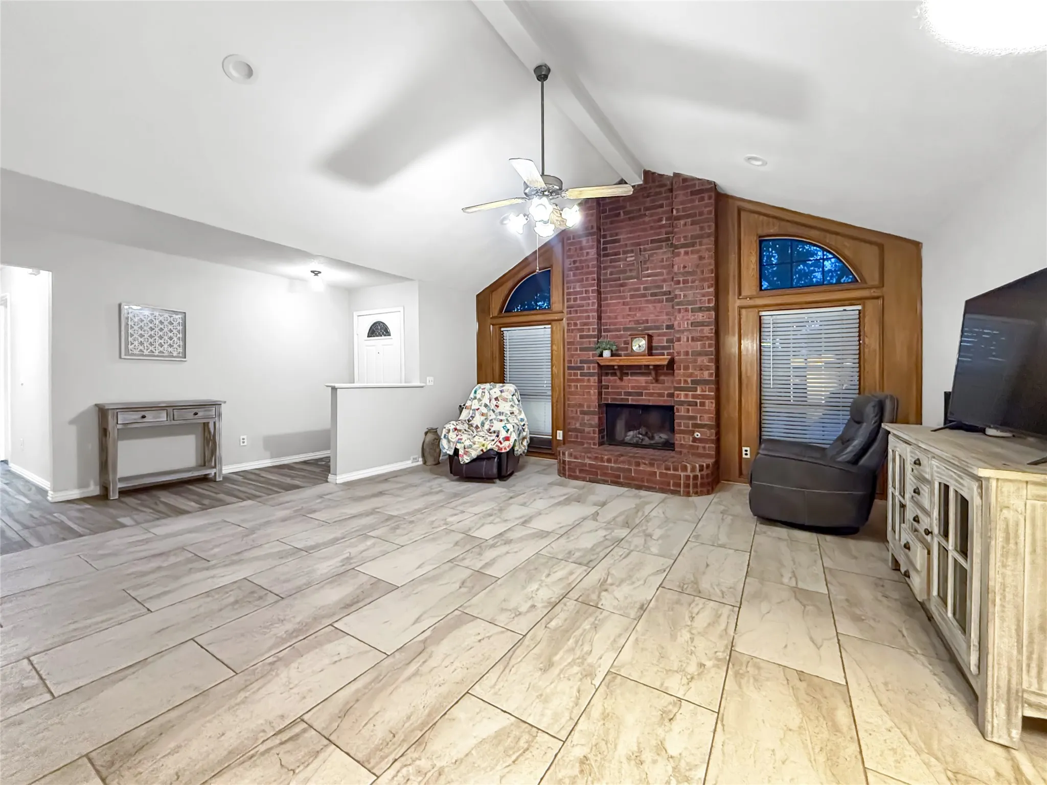 Spacious living area featuring vaulted ceilings, a brick fireplace, and wood-finish flooring