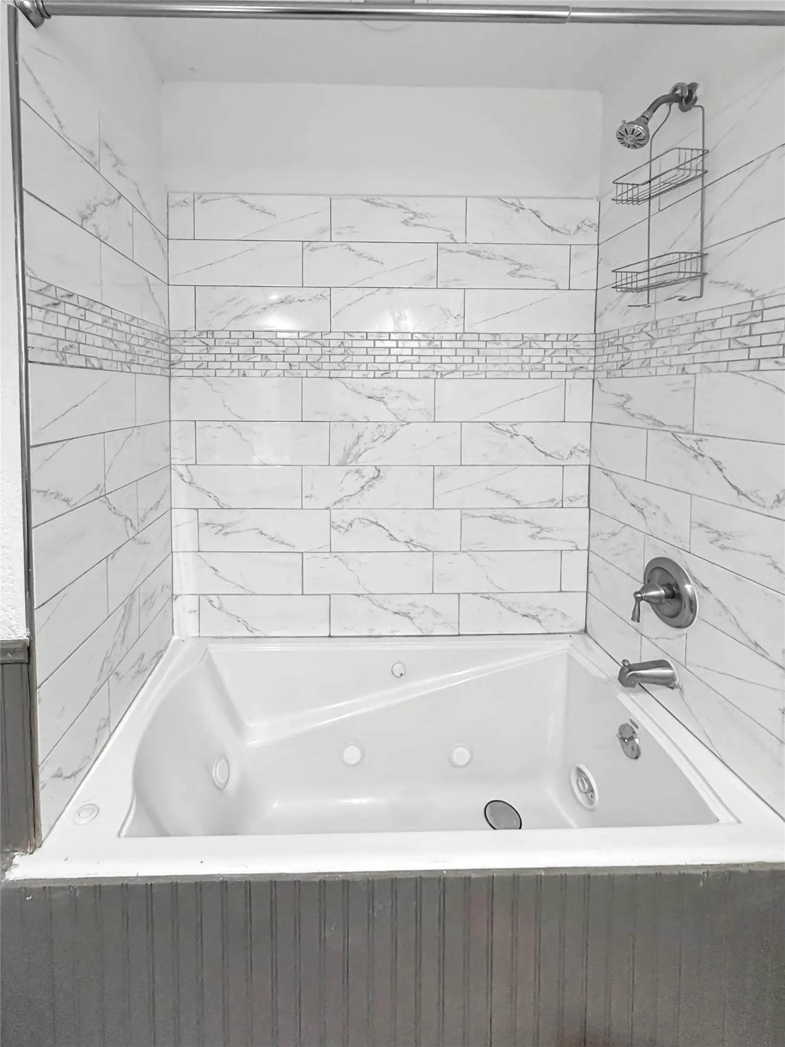 Jetted soaking tub with a brushed nickel showerhead and faucet, surrounded by white subway tile with gray veining and a decorative mosaic accent band