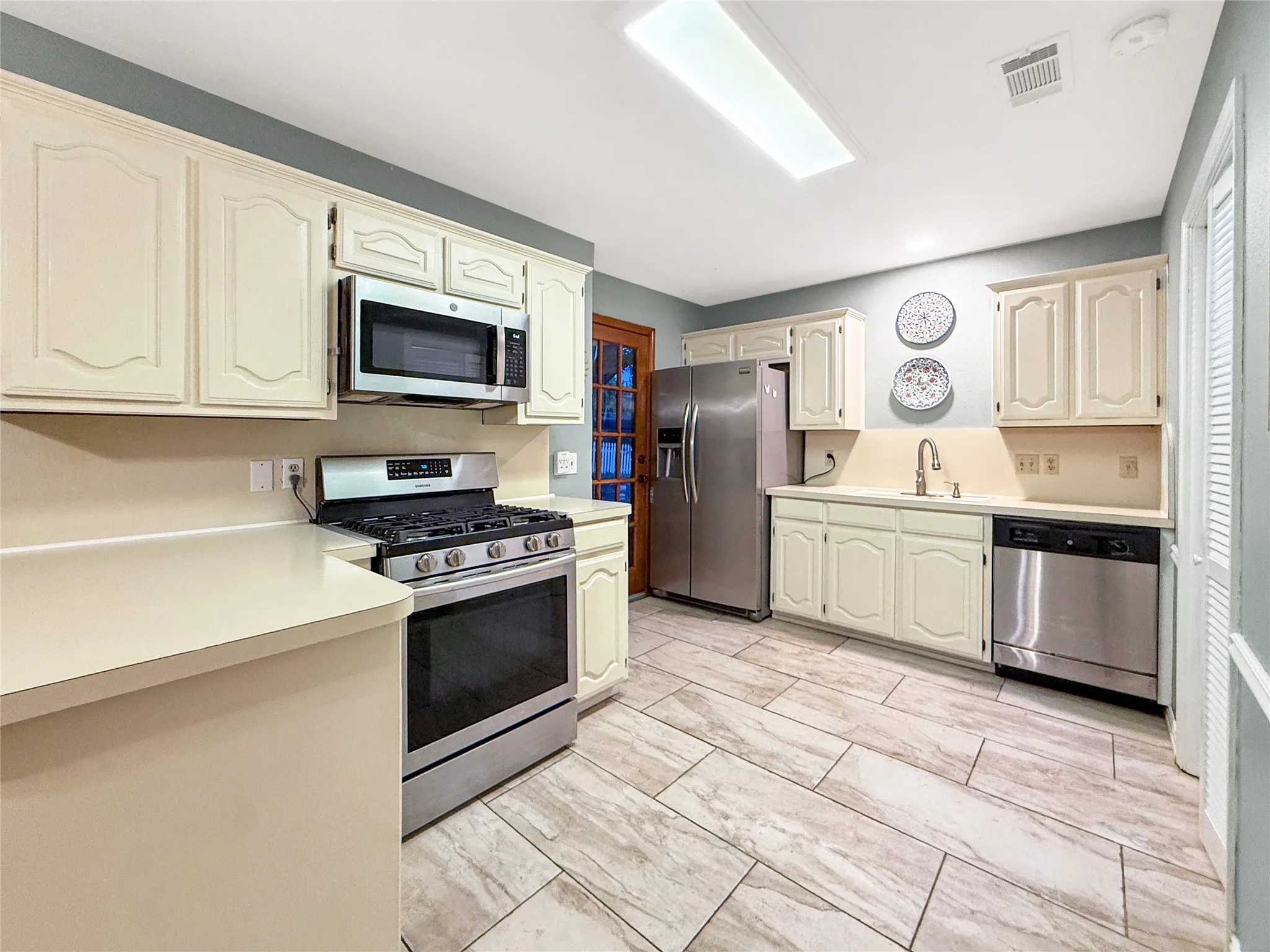 Cream-painted cabinetry, stainless steel appliances, light-toned countertops, and rectangular tile flooring