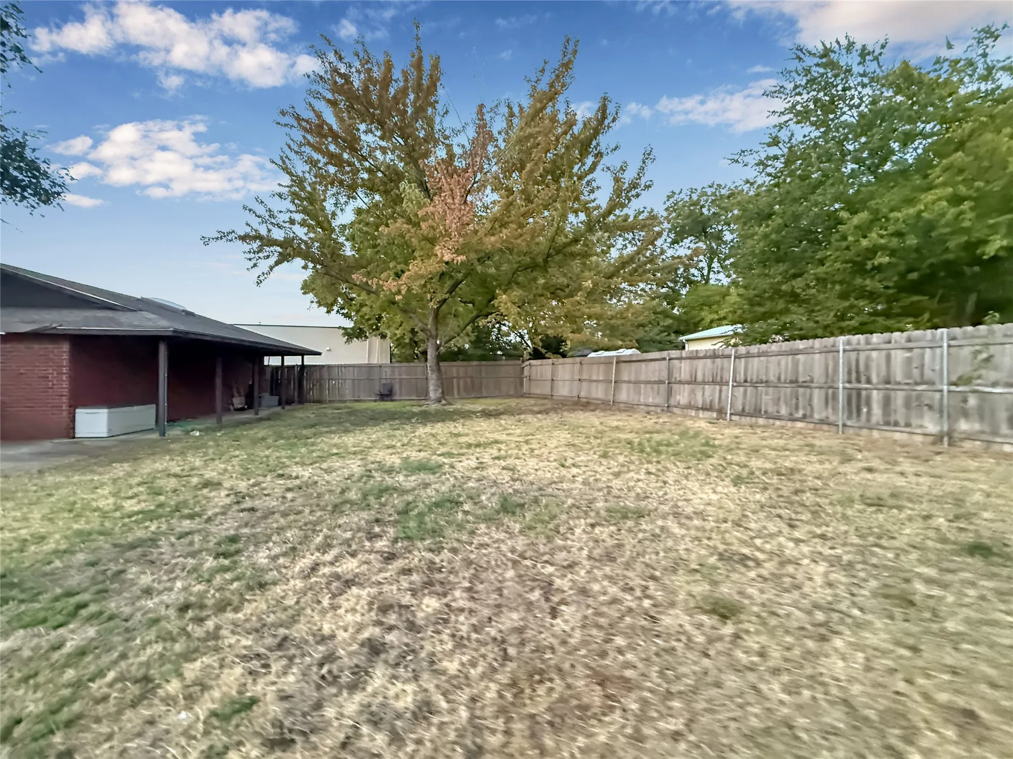 Expansive backyard featuring a wood privacy fence, mature trees, and a covered patio with a red brick exterior