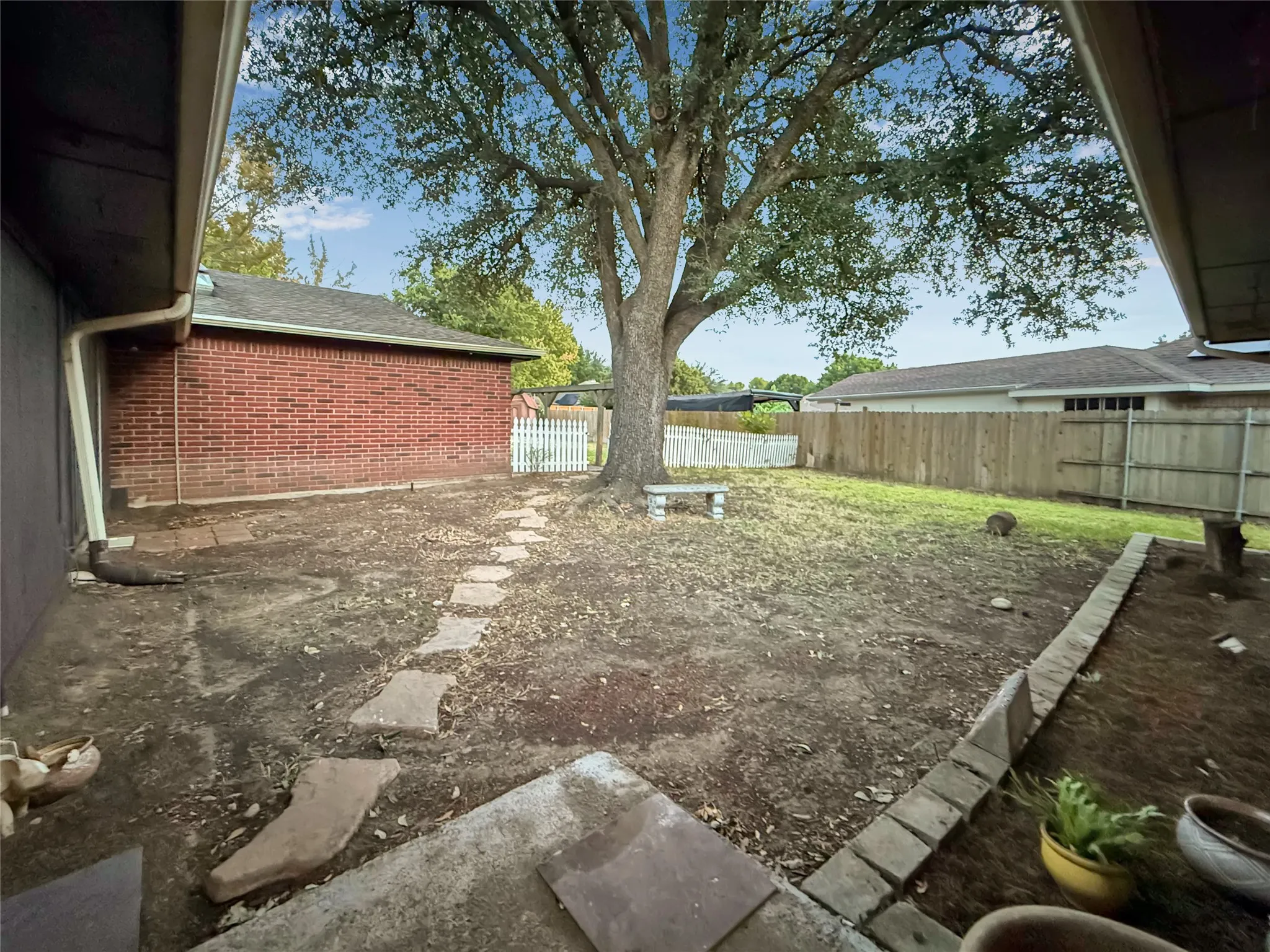 Expansive backyard featuring a mature tree, stone pathway, and a privacy fence