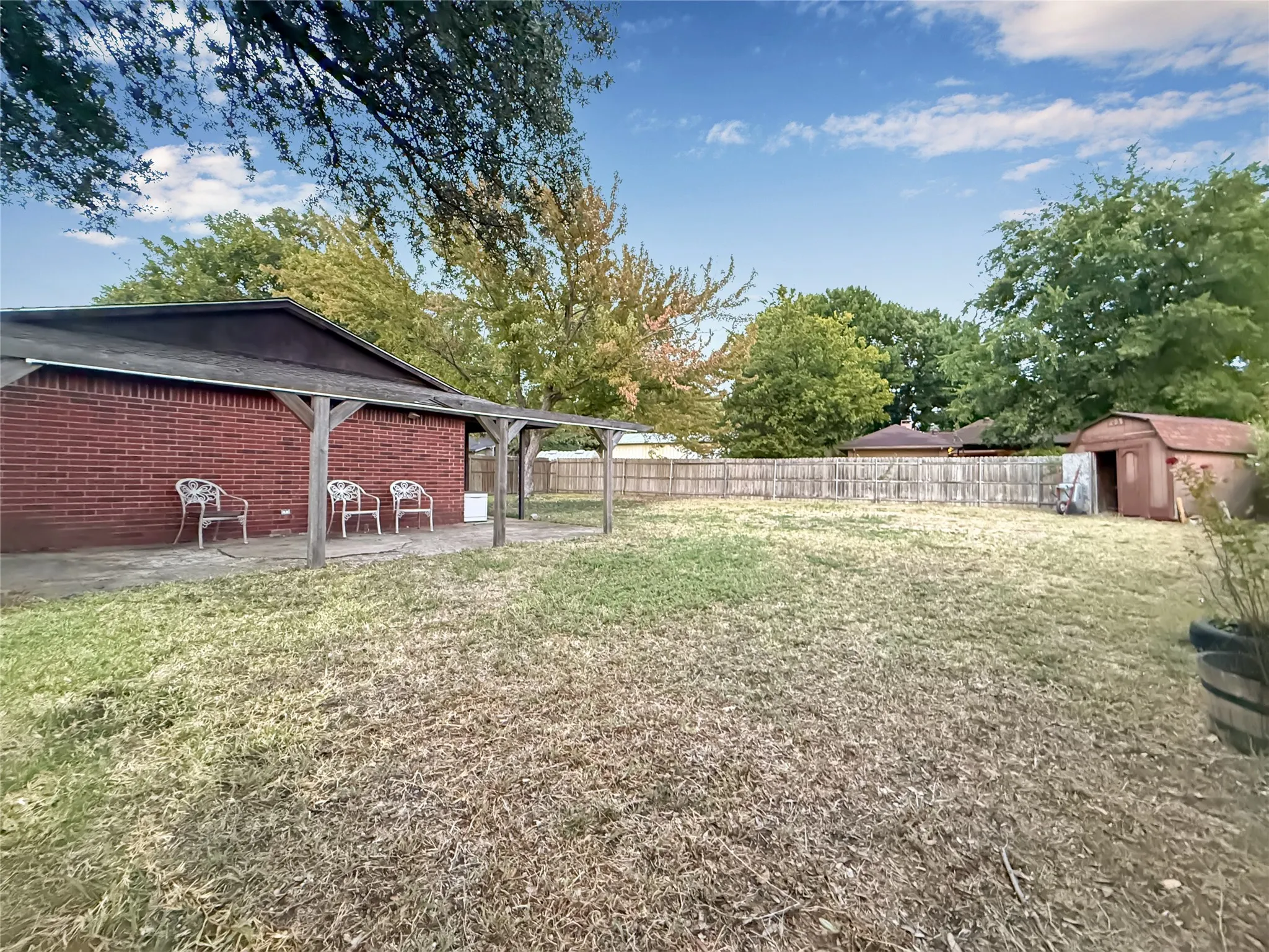 Expansive backyard featuring a brick exterior, covered patio, wood fencing, and a storage shed