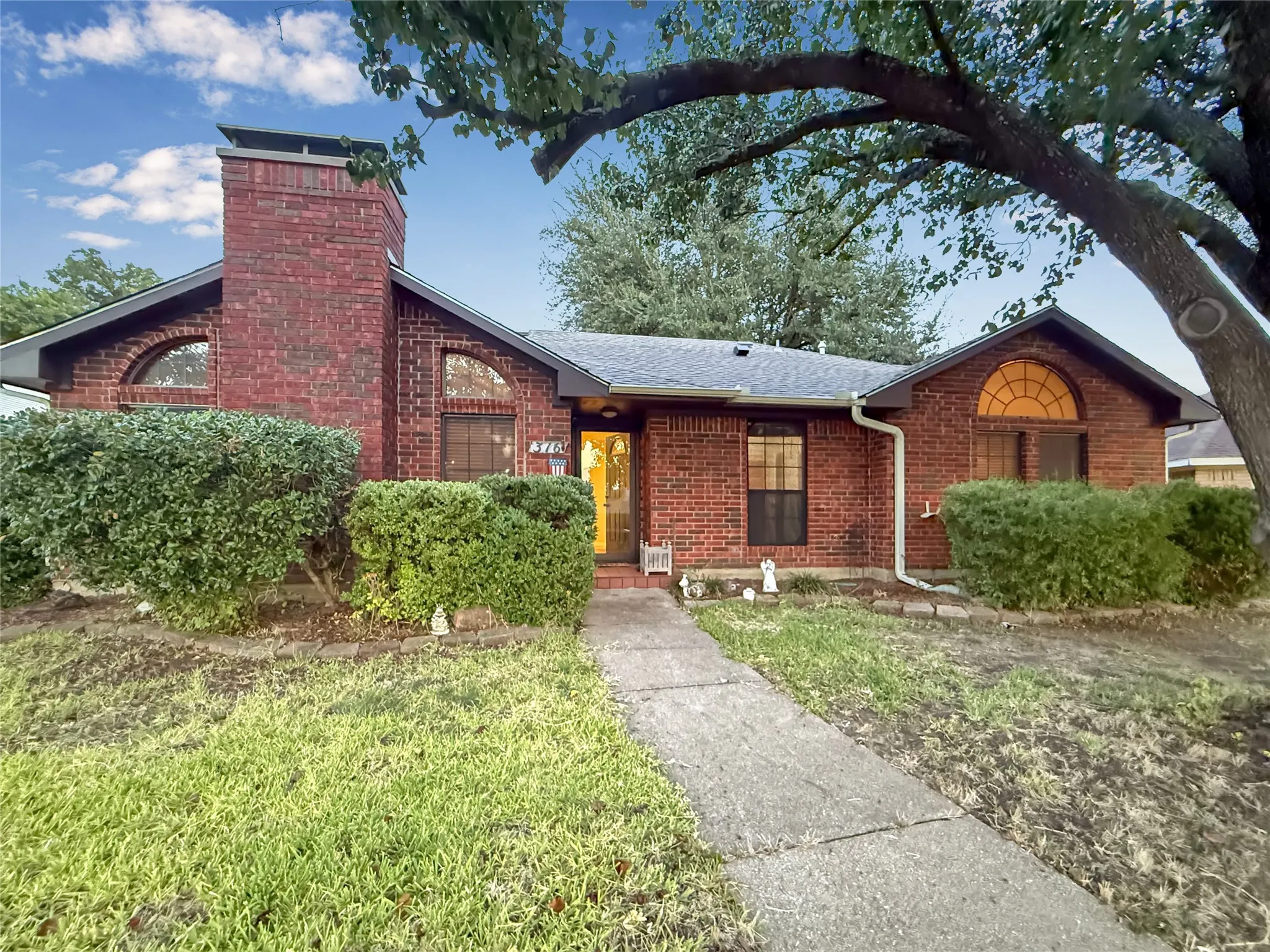 Red brick exterior with a prominent brick chimney, arched windows, and a mature tree providing natural shade