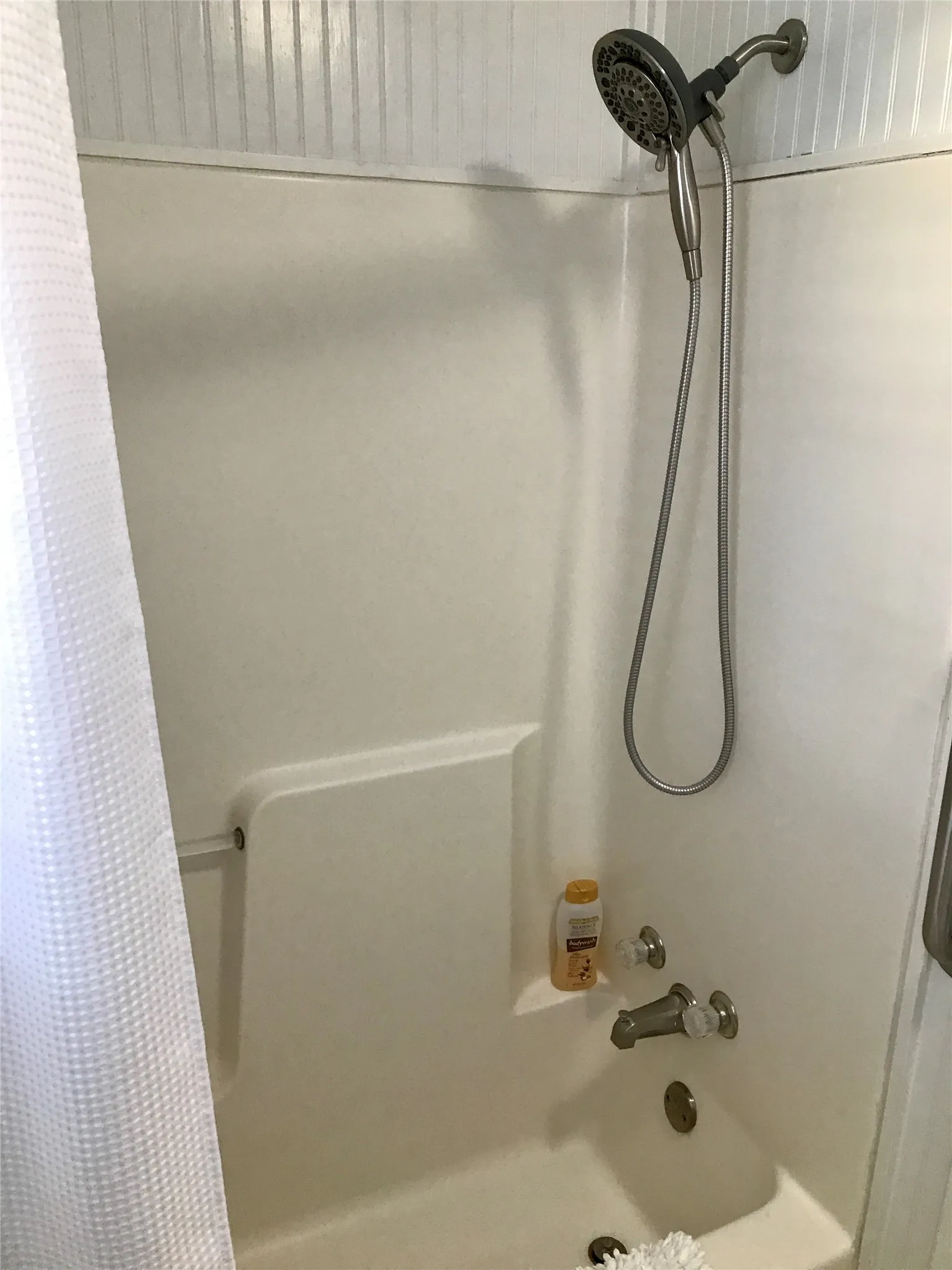 Tub and shower combination with a handheld shower head, integrated shelving, and white acrylic surround