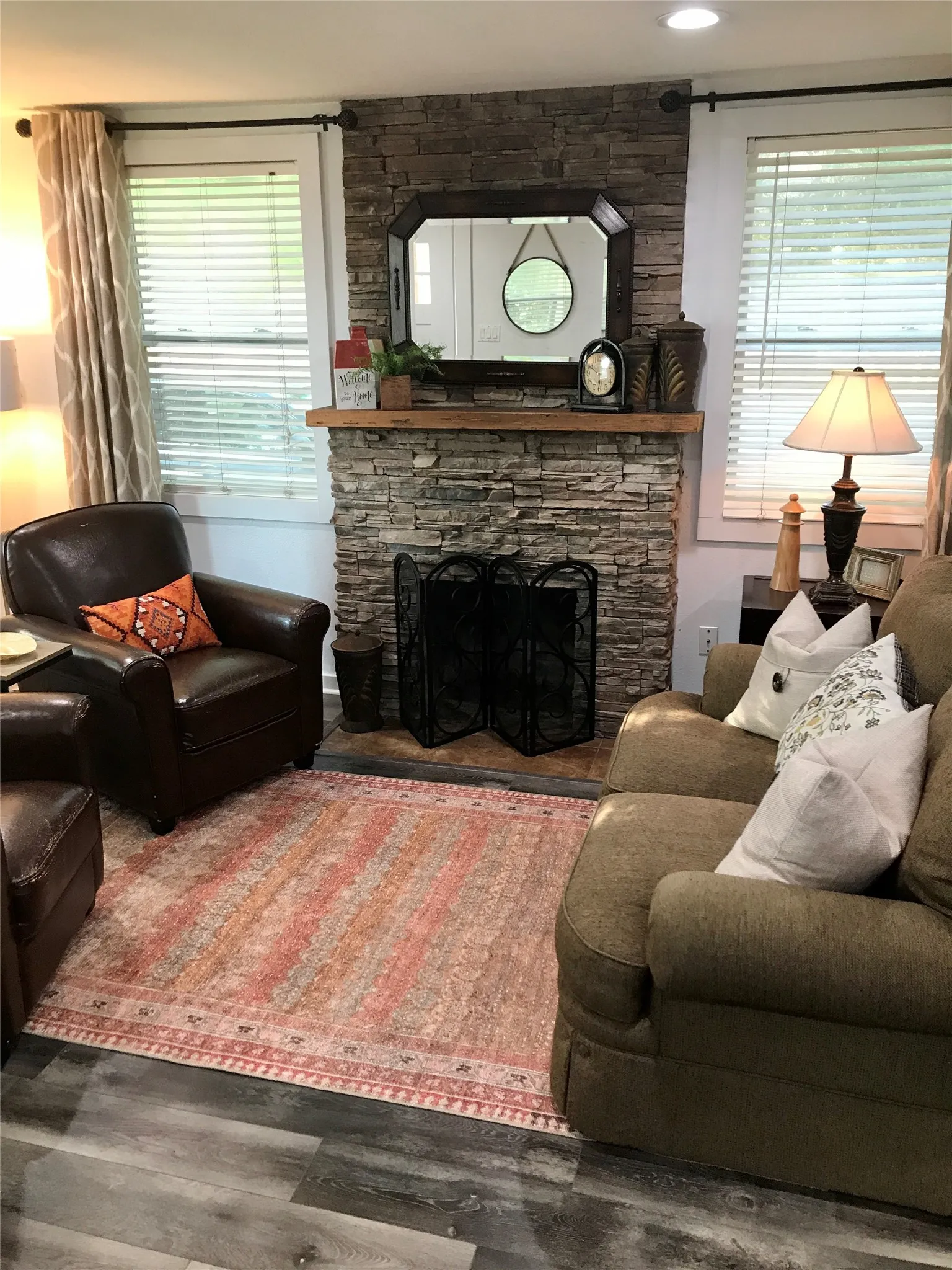 Stone-faced fireplace with a wood mantel, dark wood-finish flooring, and recessed ceiling lighting