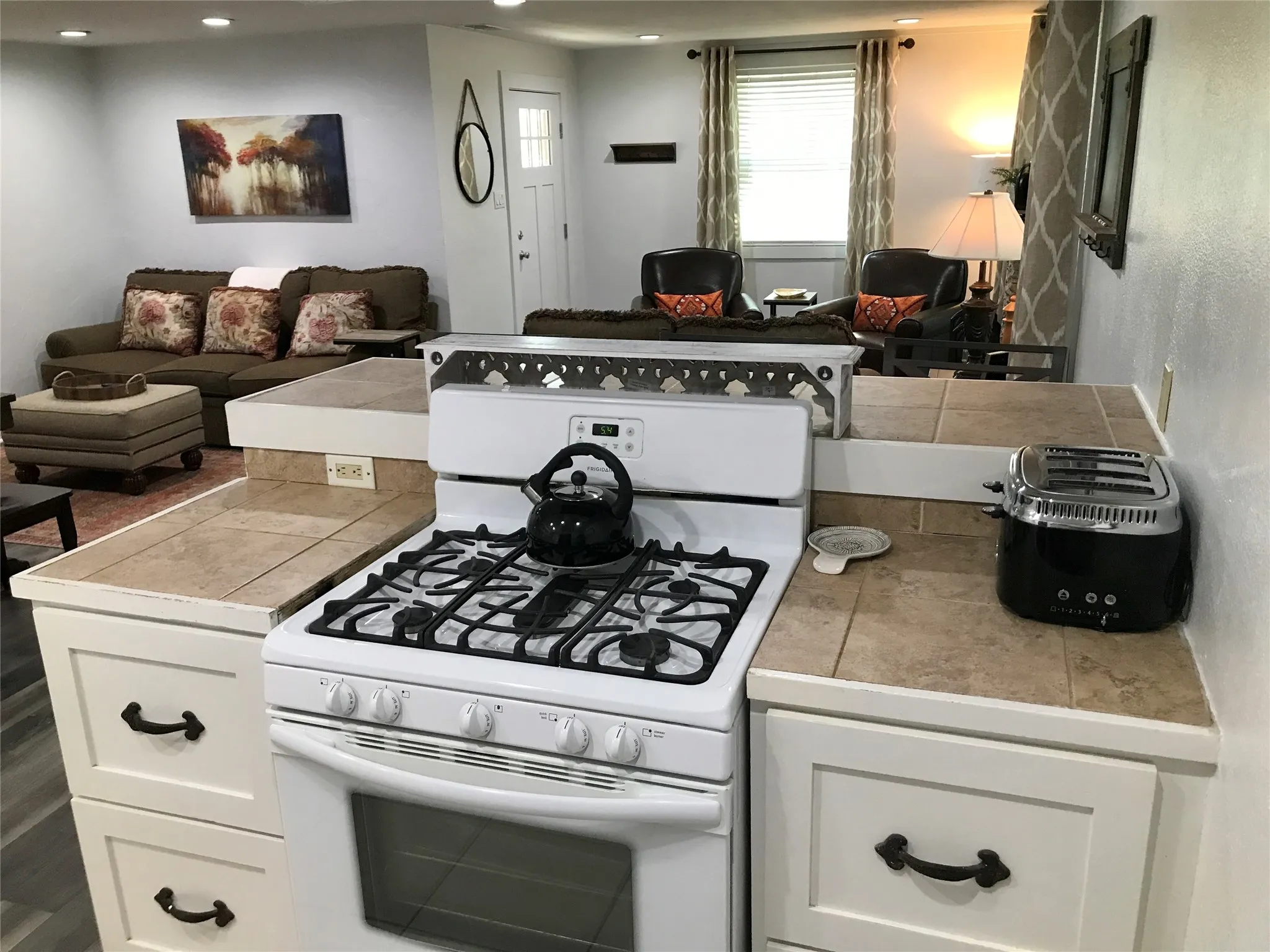 White gas range with a black grate, ceramic tile countertops, white cabinetry with dark hardware, and recessed lighting