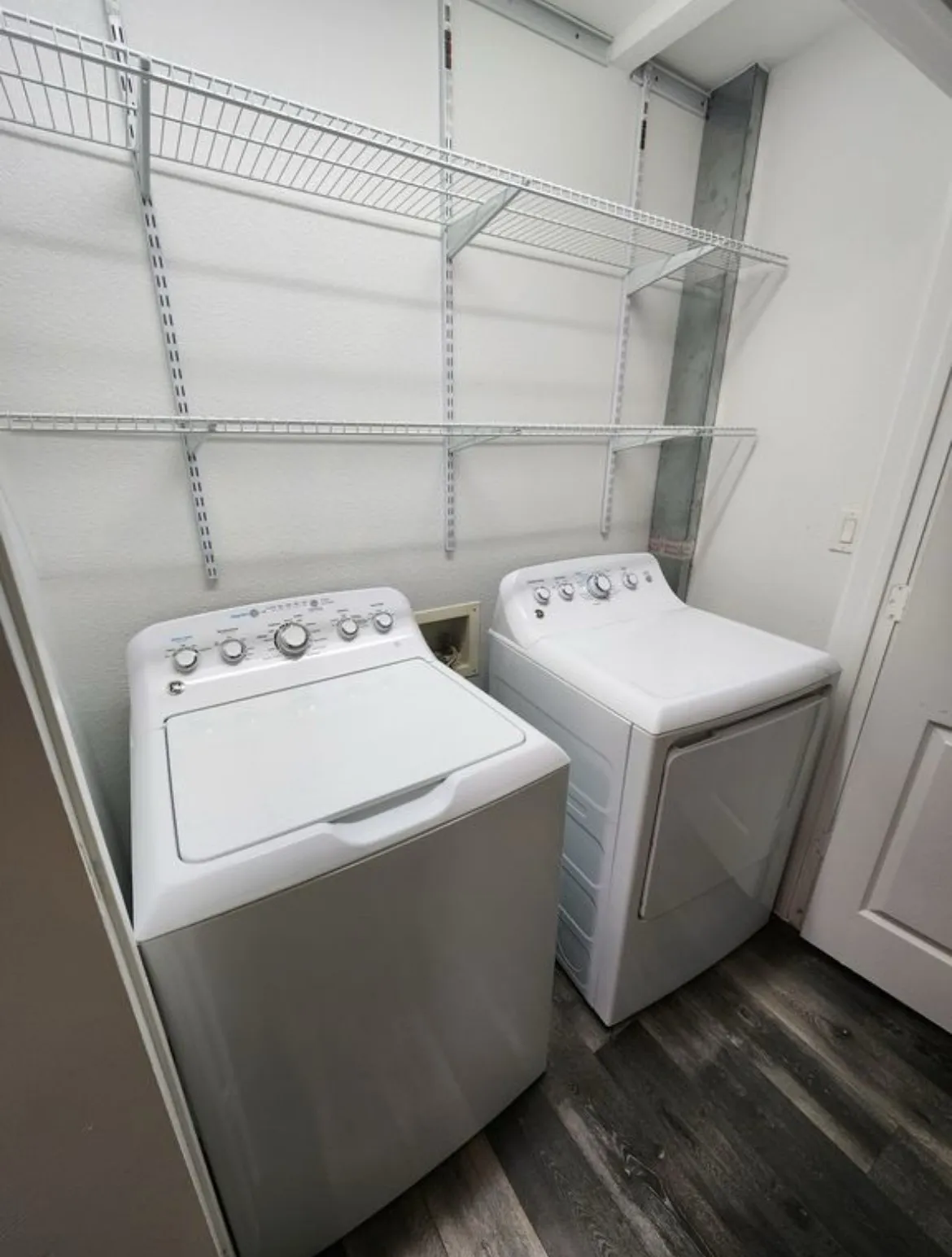 Dedicated laundry area featuring wire shelving, wood-finish flooring, a top-load washing machine, and a front-load dryer
